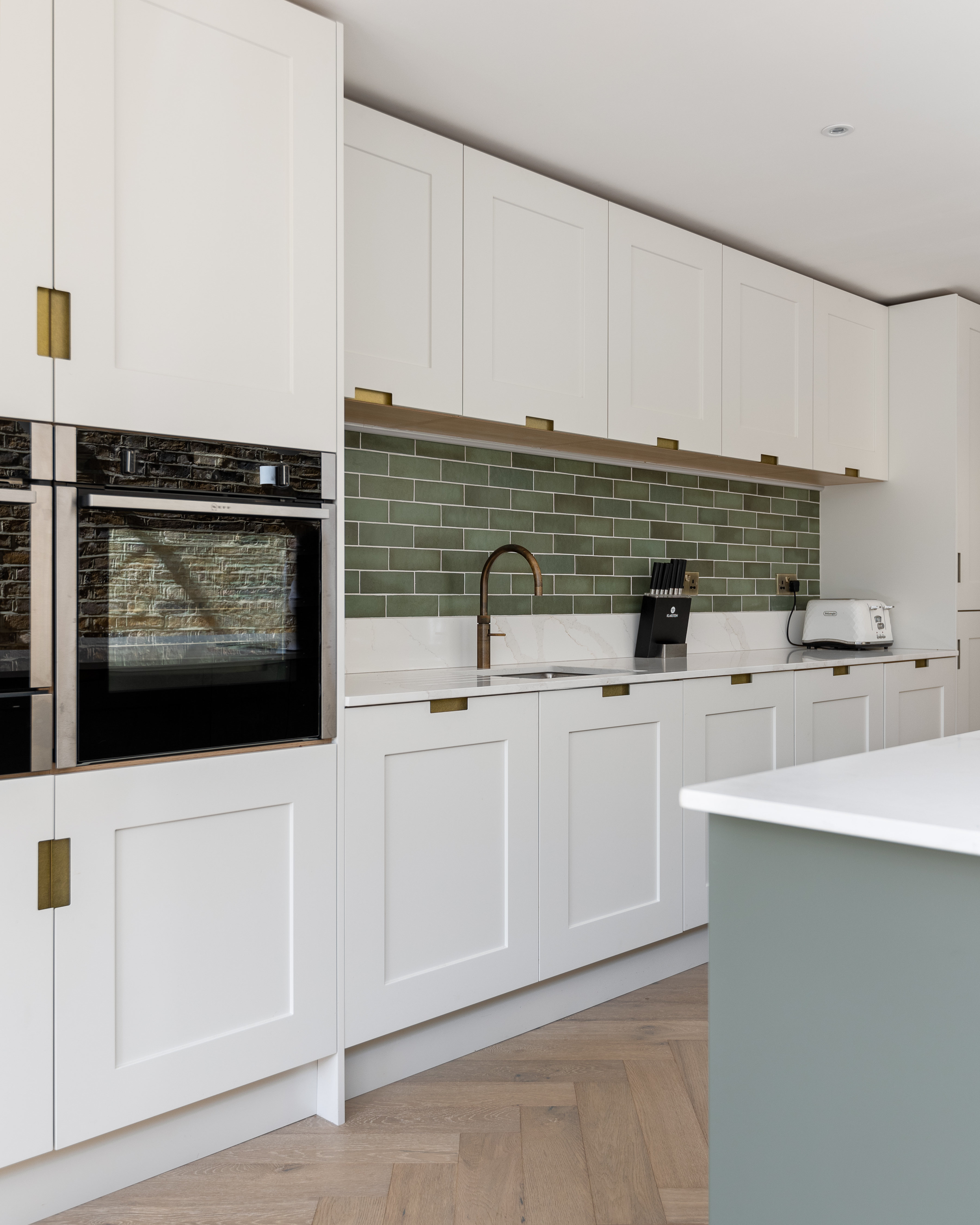 Modern kitchen design featuring white cabinetry, green subway tile backsplash, and stainless steel appliances. An Arch KBB team member is present, showcasing a stylish and functional space with a blend of contemporary and classic elements.