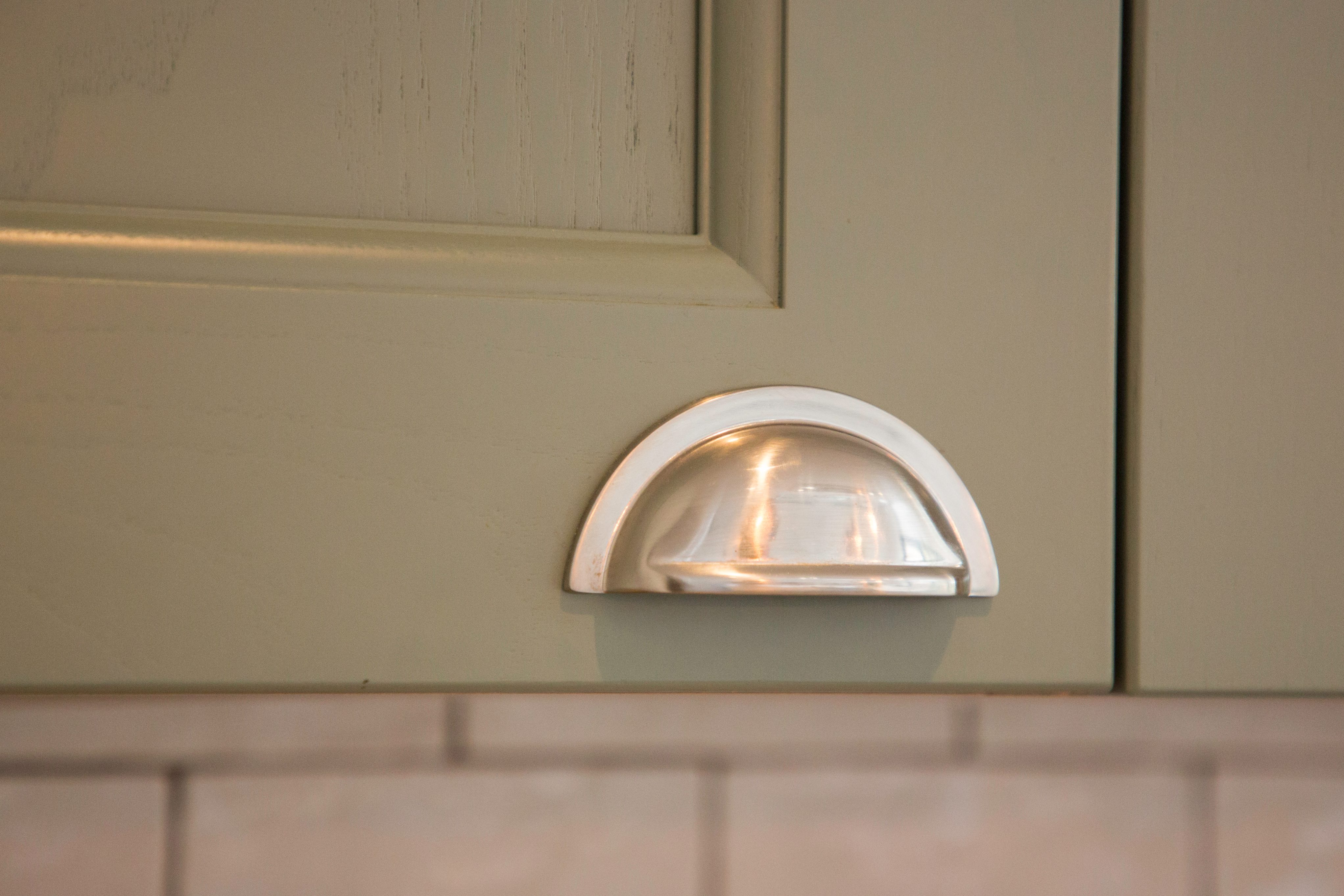Close-up of a stylish silver cup handle on a sage green kitchen cabinet door, showcasing modern design elements in interior decor.