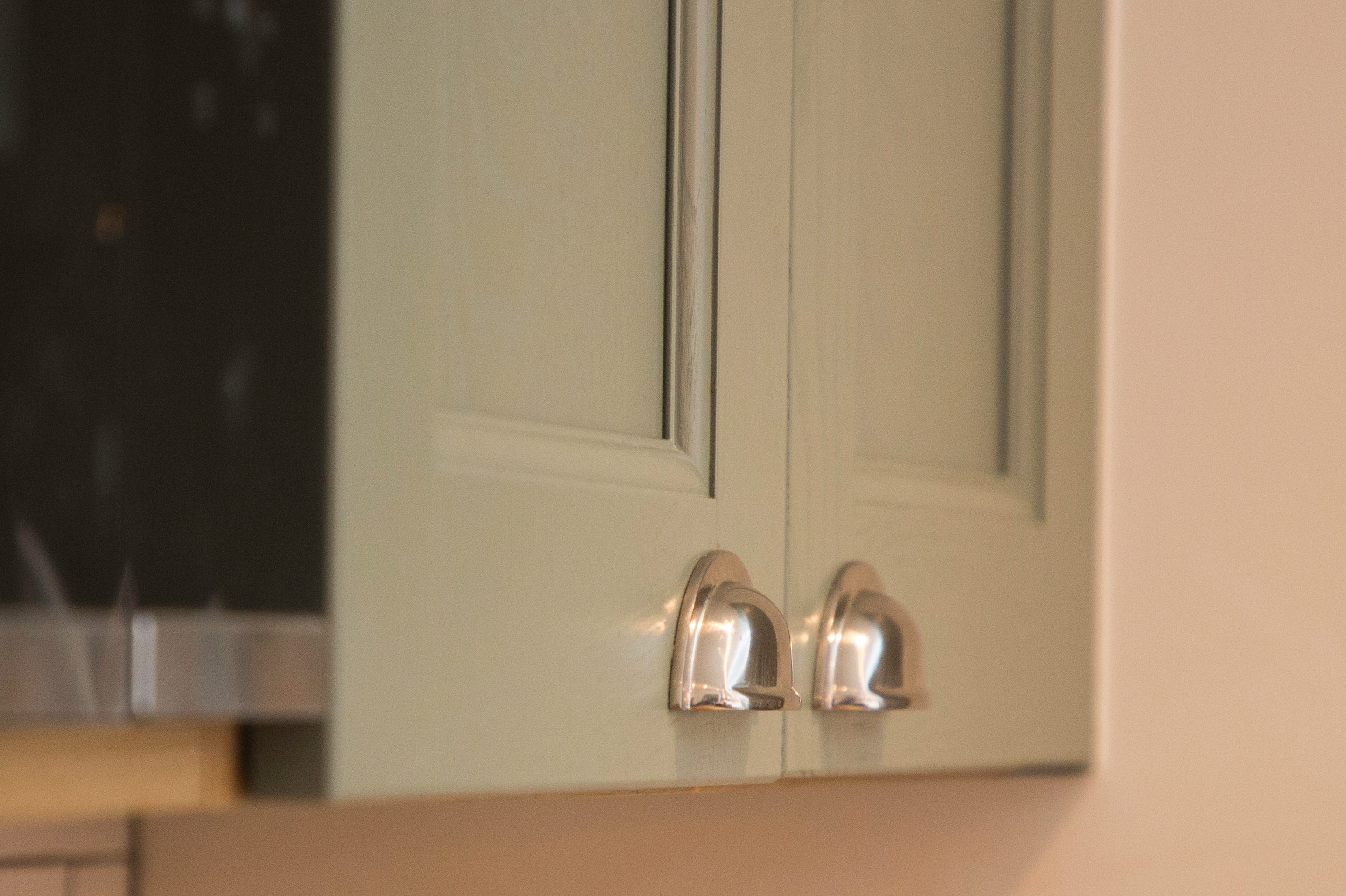 Close-up of stylish kitchen cabinet doors in a muted green finish, featuring sleek metallic handles, showcasing modern design elements. An Arch KBB team member is present, contributing to the kitchen's aesthetic appeal.