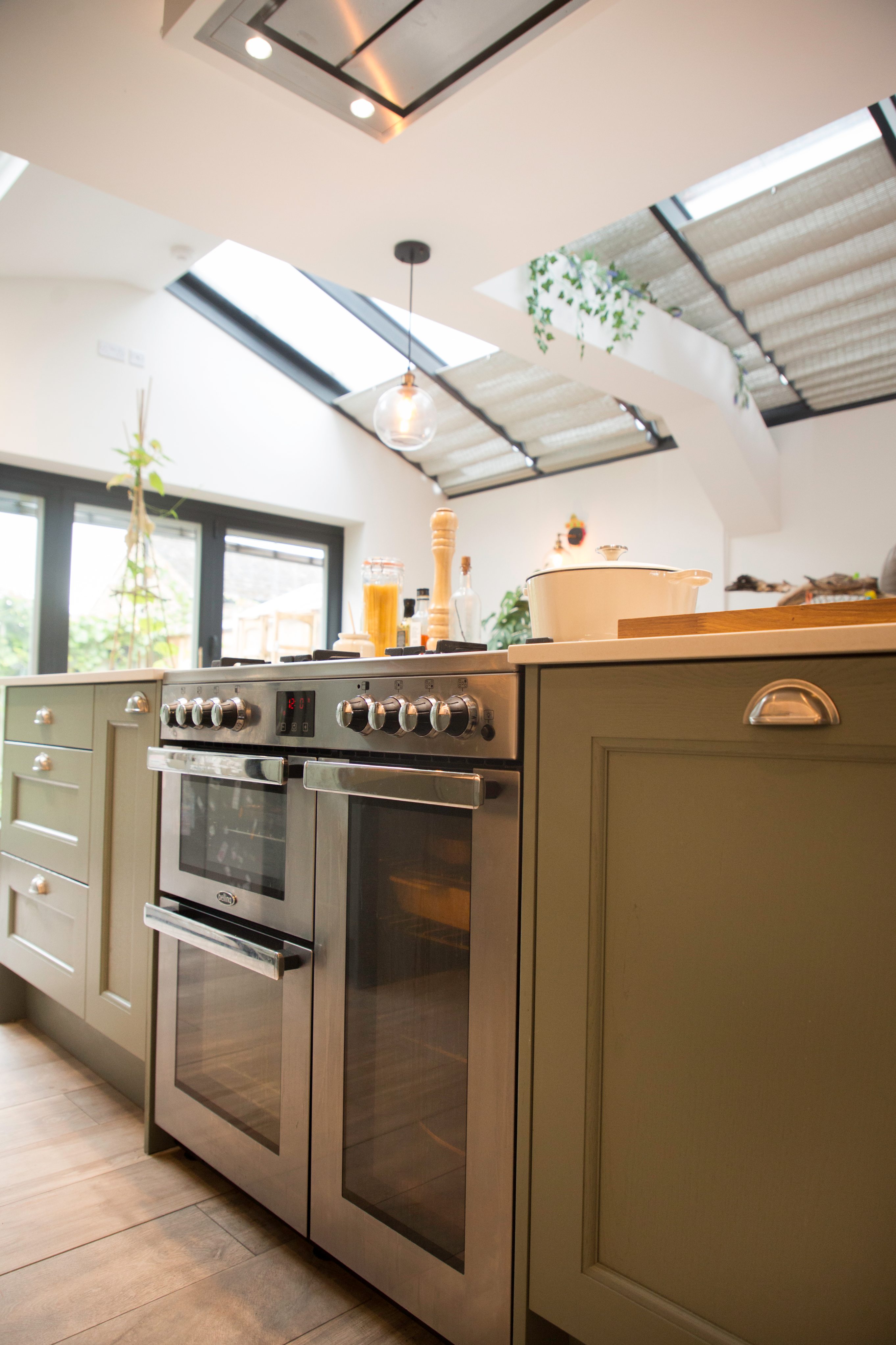 Modern kitchen featuring a stylish range cooker and cabinetry, with natural light streaming through large windows. An Arch KBB team member is present, contributing to the inviting atmosphere. The design combines functionality and aesthetics, highlighting a contemporary culinary space.