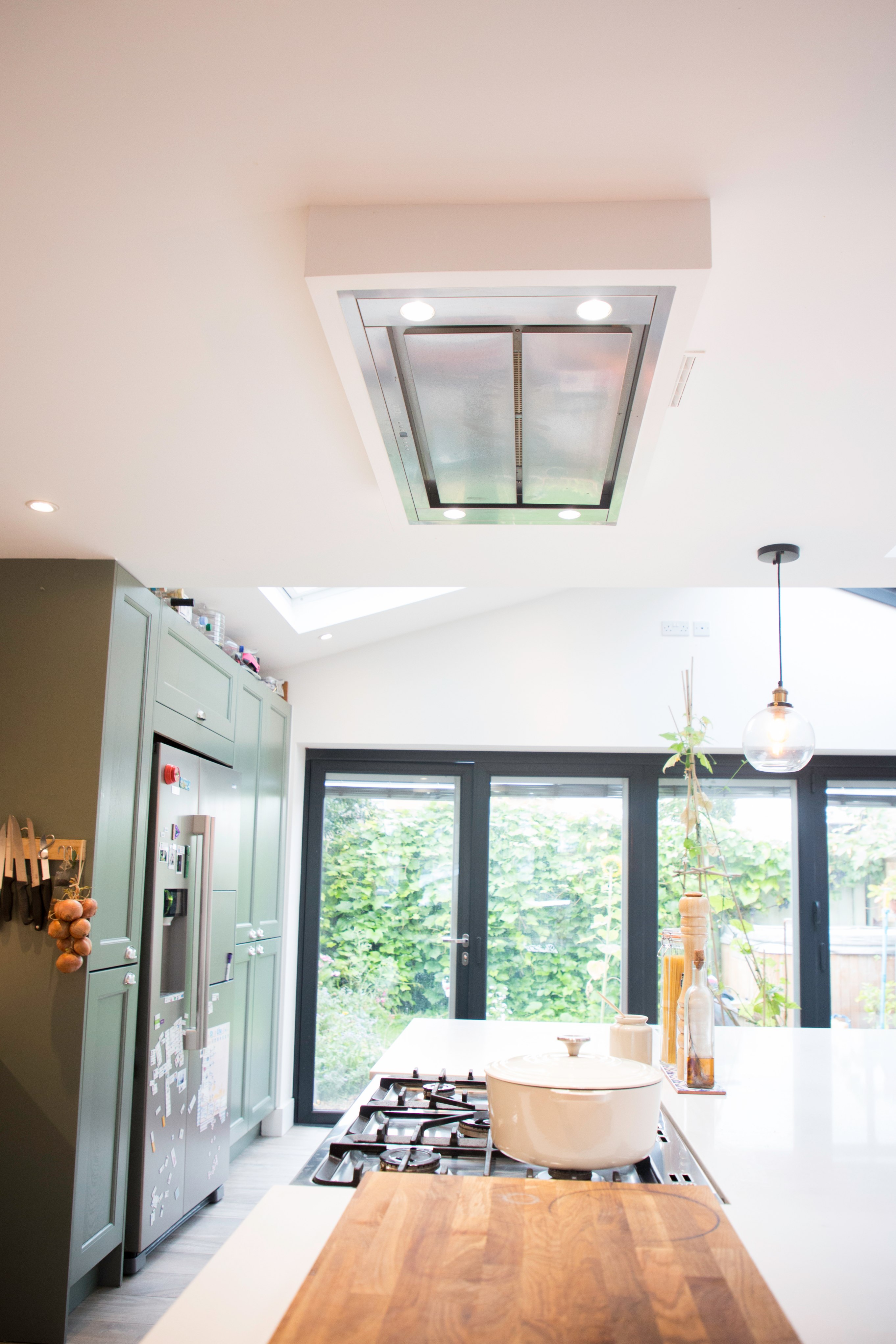Modern kitchen interior featuring a sleek extractor hood, large windows, and stylish cabinetry. An Arch KBB team member is present, enhancing the design atmosphere. Natural light floods the space, highlighting the greenery outside.