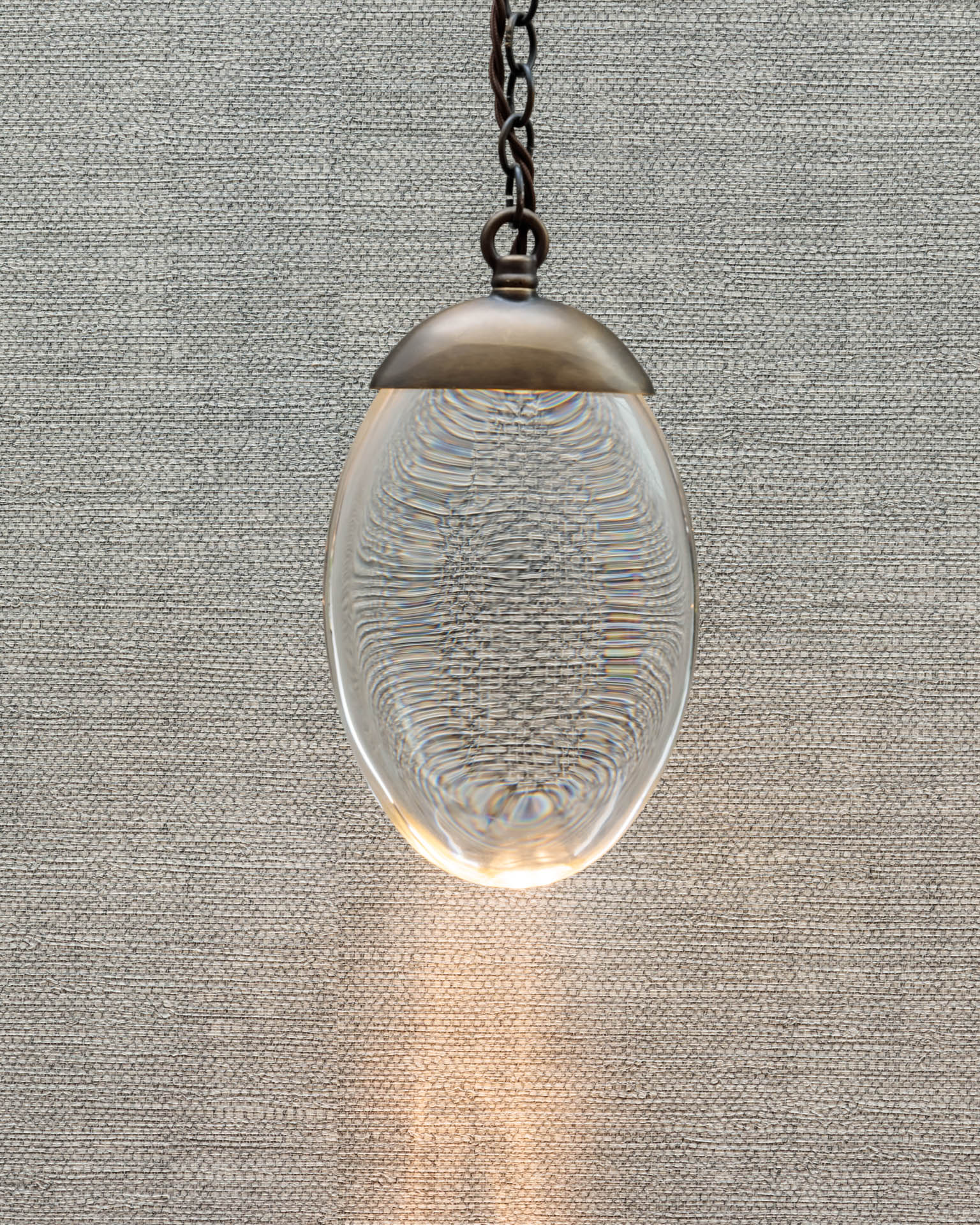 Hanging pendant light featuring a clear, oval glass design with intricate patterns, suspended against a textured grey background. An Arch KBB team member is present, showcasing the lighting fixture in a stylish setting.