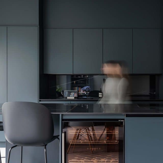 Modern kitchen interior featuring sleek grey cabinetry and a dark stone countertop. An Arch KBB team member is seen in motion, adding a dynamic element to the serene space. The design showcases contemporary appliances and minimalist decor, emphasising functionality and style.