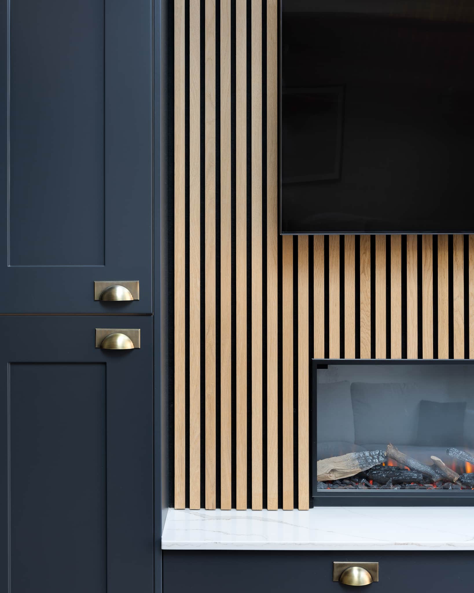 Modern interior design featuring a vertical slatted wood wall, elegant cabinetry with brass handles, and a minimalist television above a contemporary fireplace. An Arch KBB team member is present, highlighting the stylish integration of warmth and sophistication in the living space.