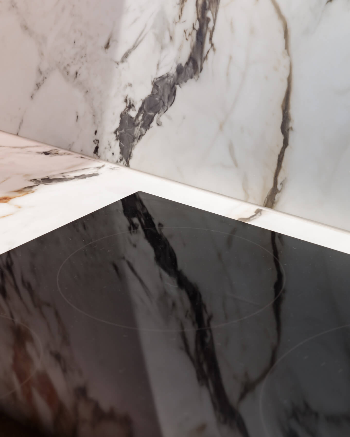 Close-up image of a sleek black induction cooktop set against a backdrop of elegant marble surfaces, showcasing a modern kitchen aesthetic. An Arch KBB team member is present, contributing to the design setup.