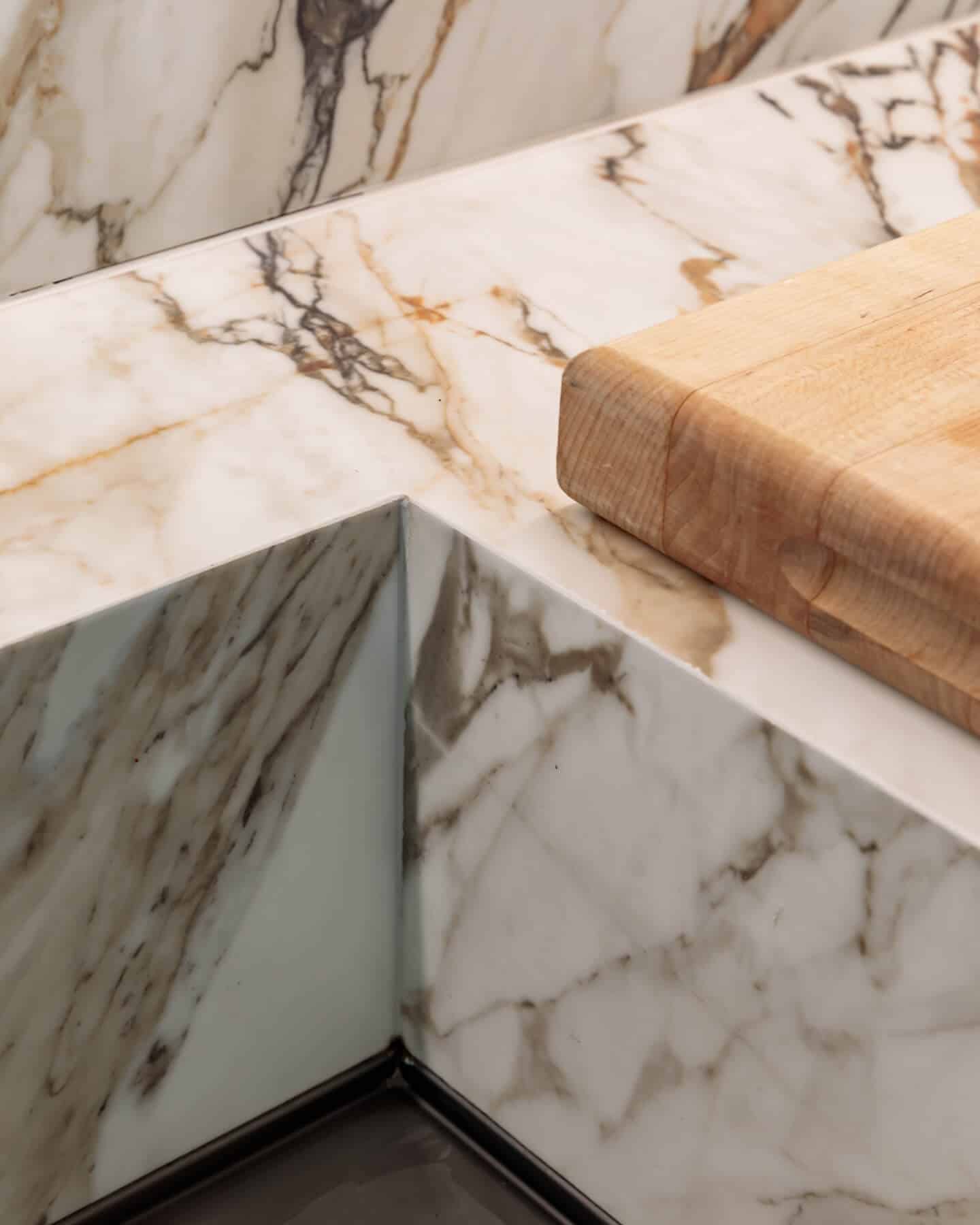 Close-up of a marble countertop featuring intricate veining, complemented by a wooden chopping board. The image showcases the elegant design and texture of the marble, ideal for kitchen aesthetics. An Arch KBB team member is present, highlighting the craftsmanship involved in kitchen design.