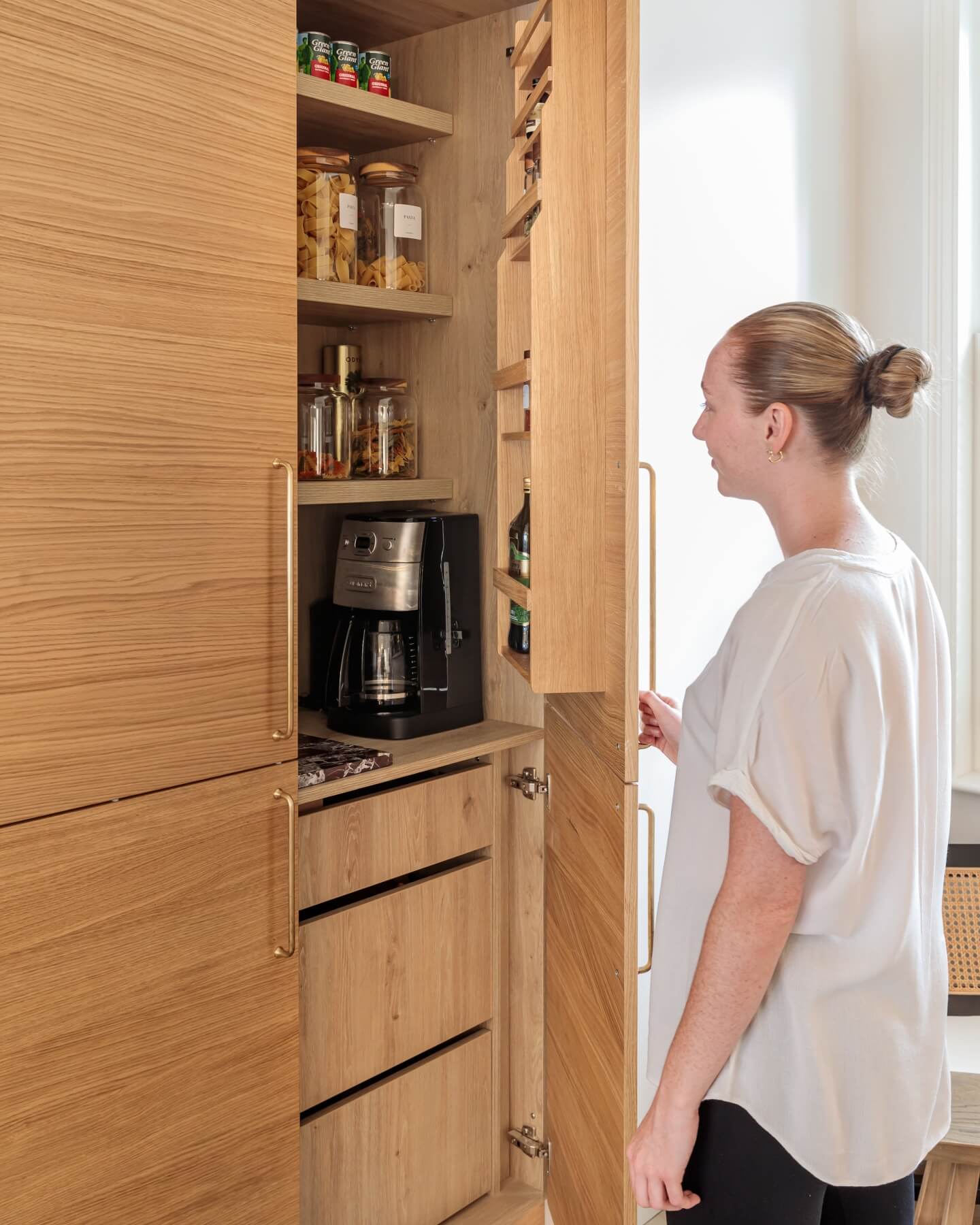 Arch KBB team member interacting with a stylish wooden kitchen cabinet, featuring a coffee maker and jars of ingredients, showcasing modern kitchen design and functionality.