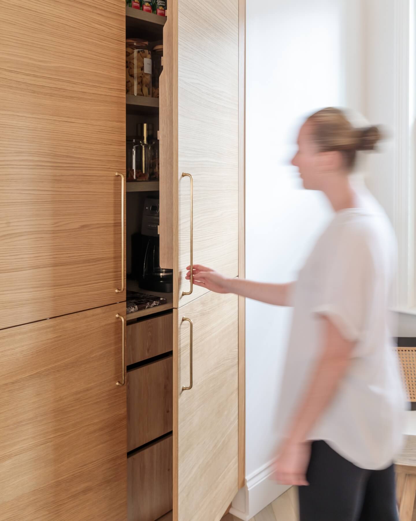 Arch KBB team member interacting with modern wooden cabinetry, featuring elegant brass handles, in a stylish kitchen setting. The image captures the seamless blend of functionality and design in contemporary home interiors.