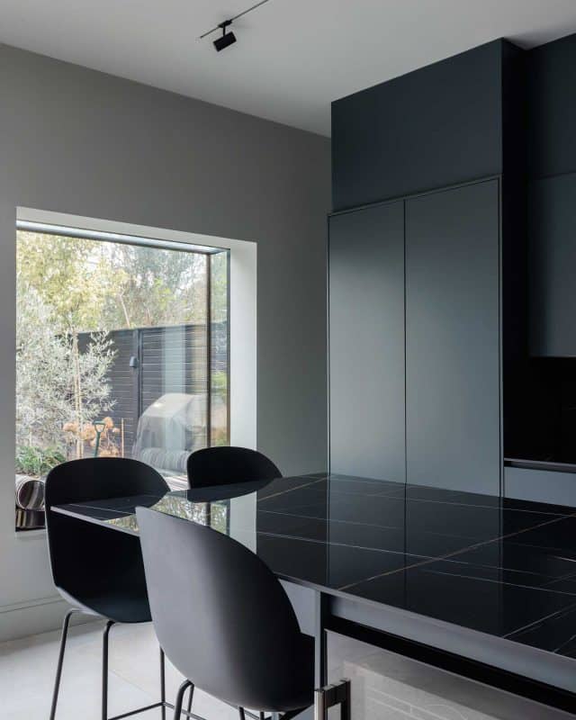 Modern kitchen interior featuring a sleek black dining table and stylish chairs, with a large window providing natural light and a view of the garden. Arch KBB team member present, showcasing contemporary design elements and minimalist aesthetics.