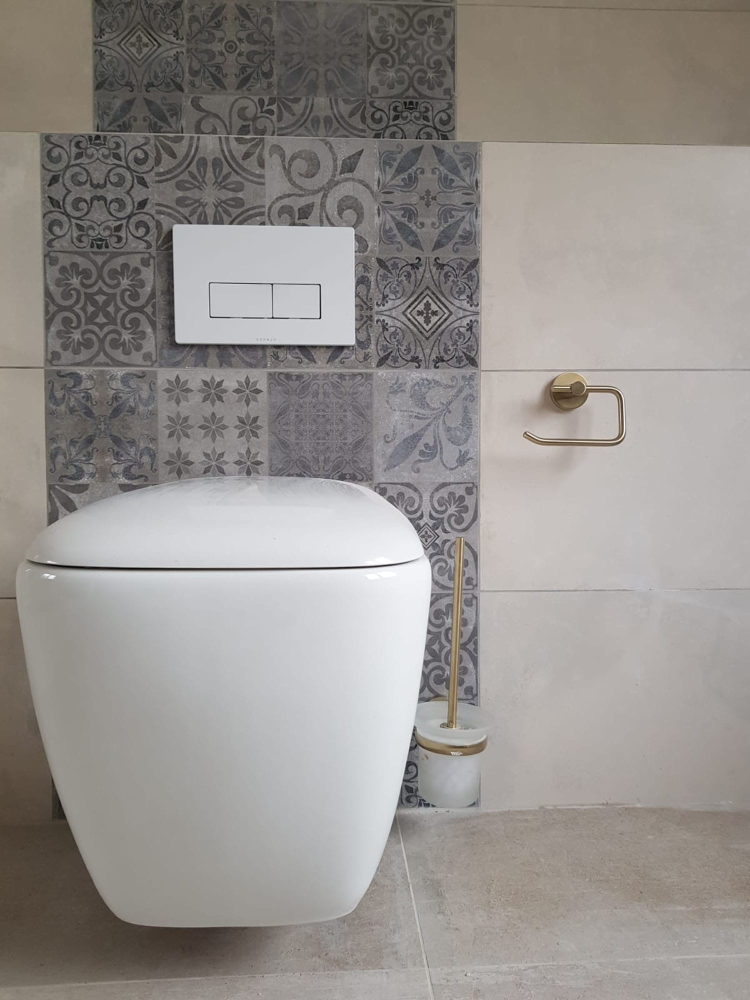 Modern bathroom featuring a white toilet, stylish patterned wall tiles, and a gold toilet roll holder. The design reflects contemporary aesthetics with a clean and elegant look.