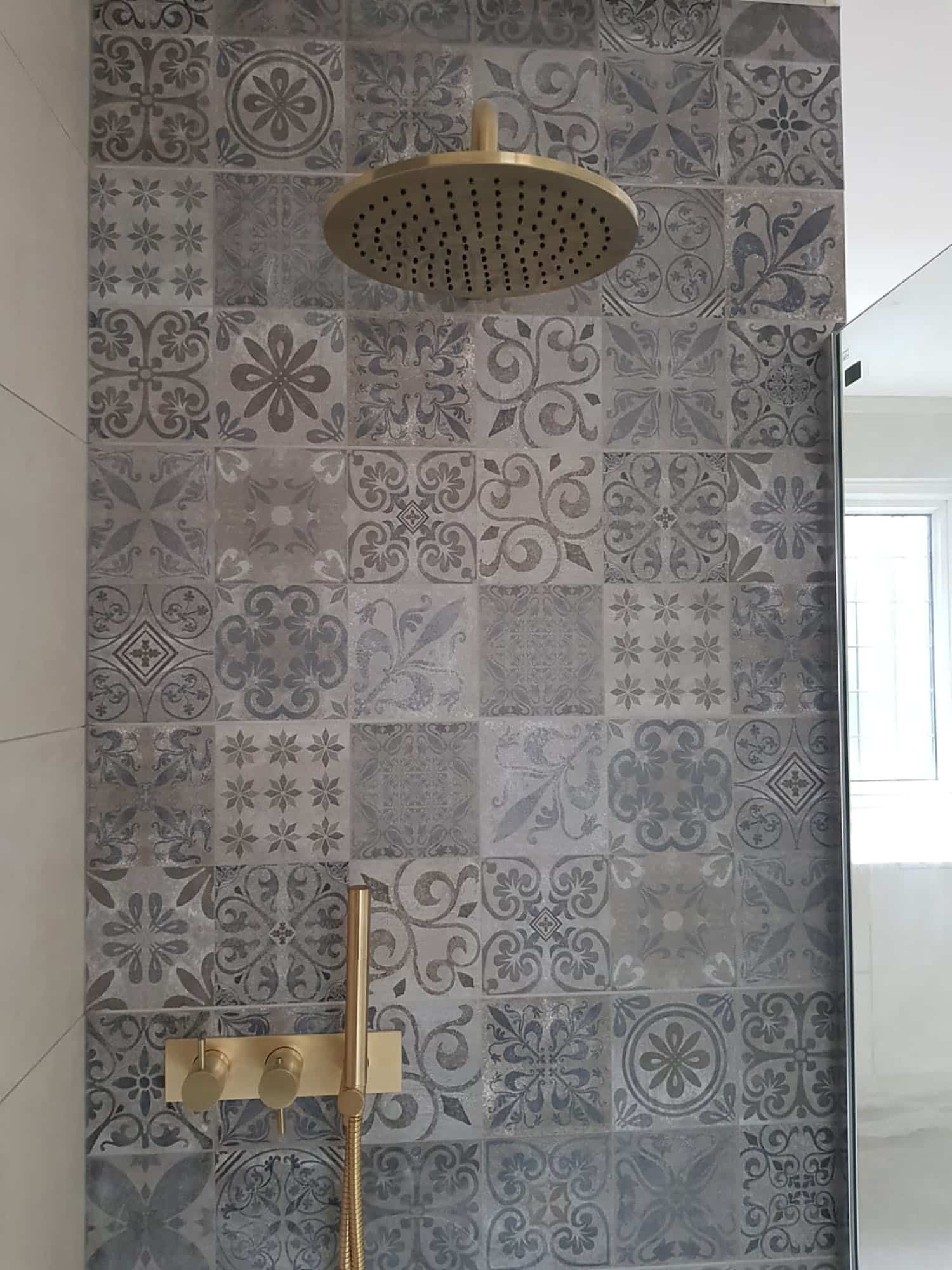 Alt text: Decorative patterned tiles in shades of grey covering a bathroom wall, featuring intricate designs and textures. An Arch KBB team member is present, enhancing the design aesthetic of the space.
