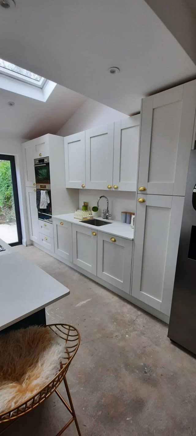 Modern kitchen design featuring sleek white cabinetry with gold handles, integrated appliances, and a minimalist sink area. An Arch KBB team member is present, showcasing a stylish and functional kitchen space.