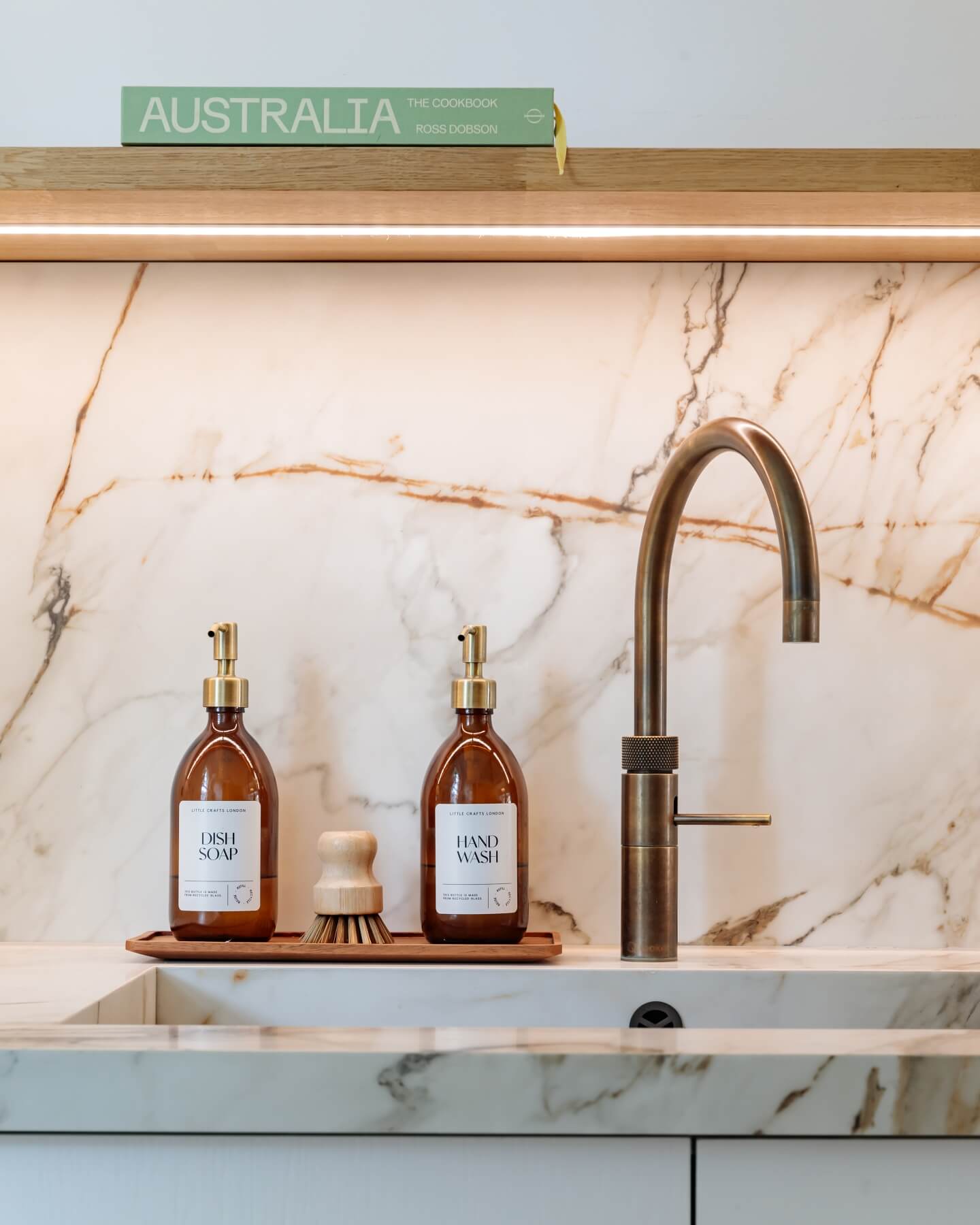 Arch KBB team member demonstrating a stylish kitchen sink area featuring elegant dish soap and hand wash dispensers on a wooden tray, complemented by a modern tap against a beautiful marble backdrop.