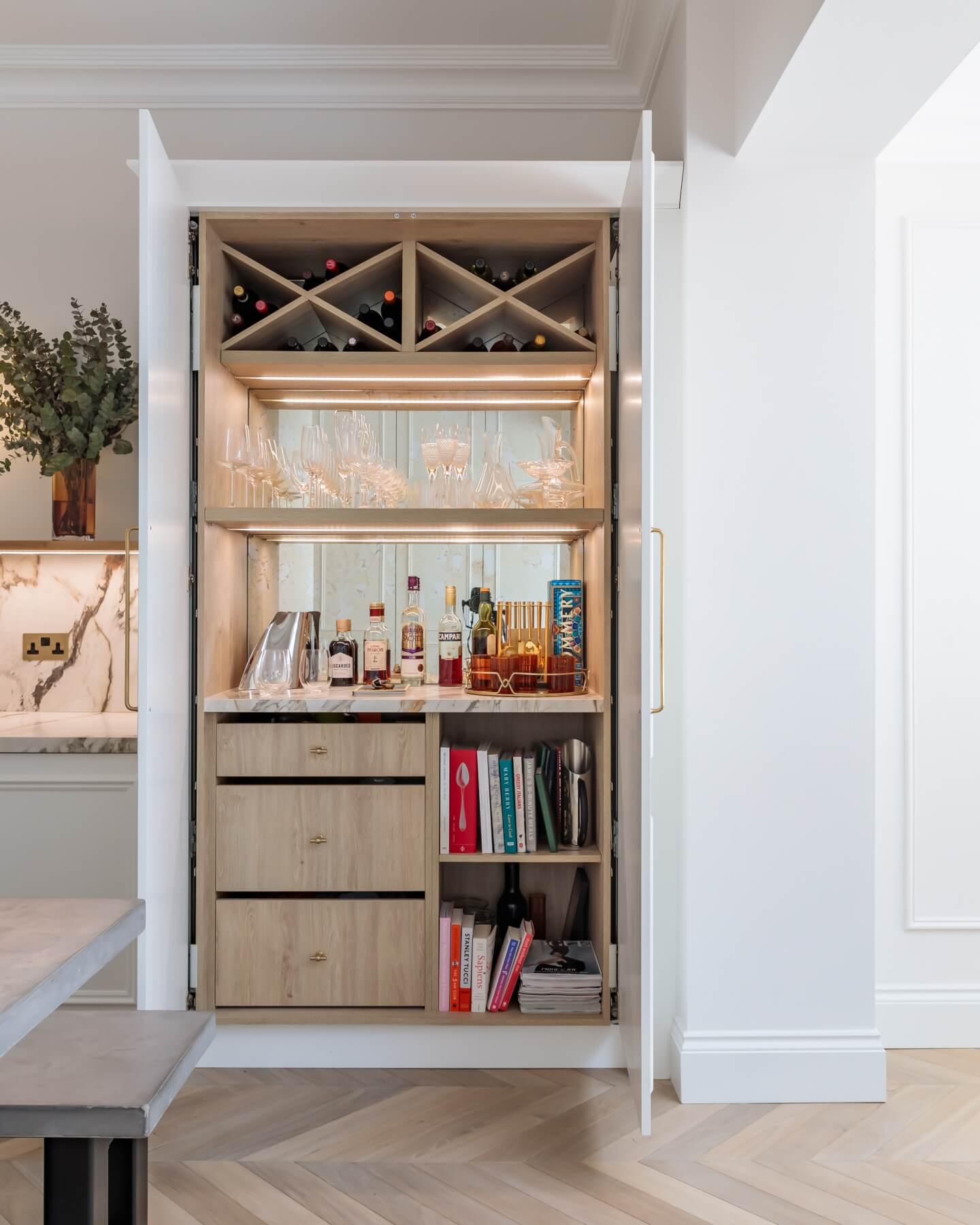 A stylish home bar featuring a wine rack, glass storage, and a selection of spirits, with neatly arranged shelves for books and barware, designed by an Arch KBB team member.