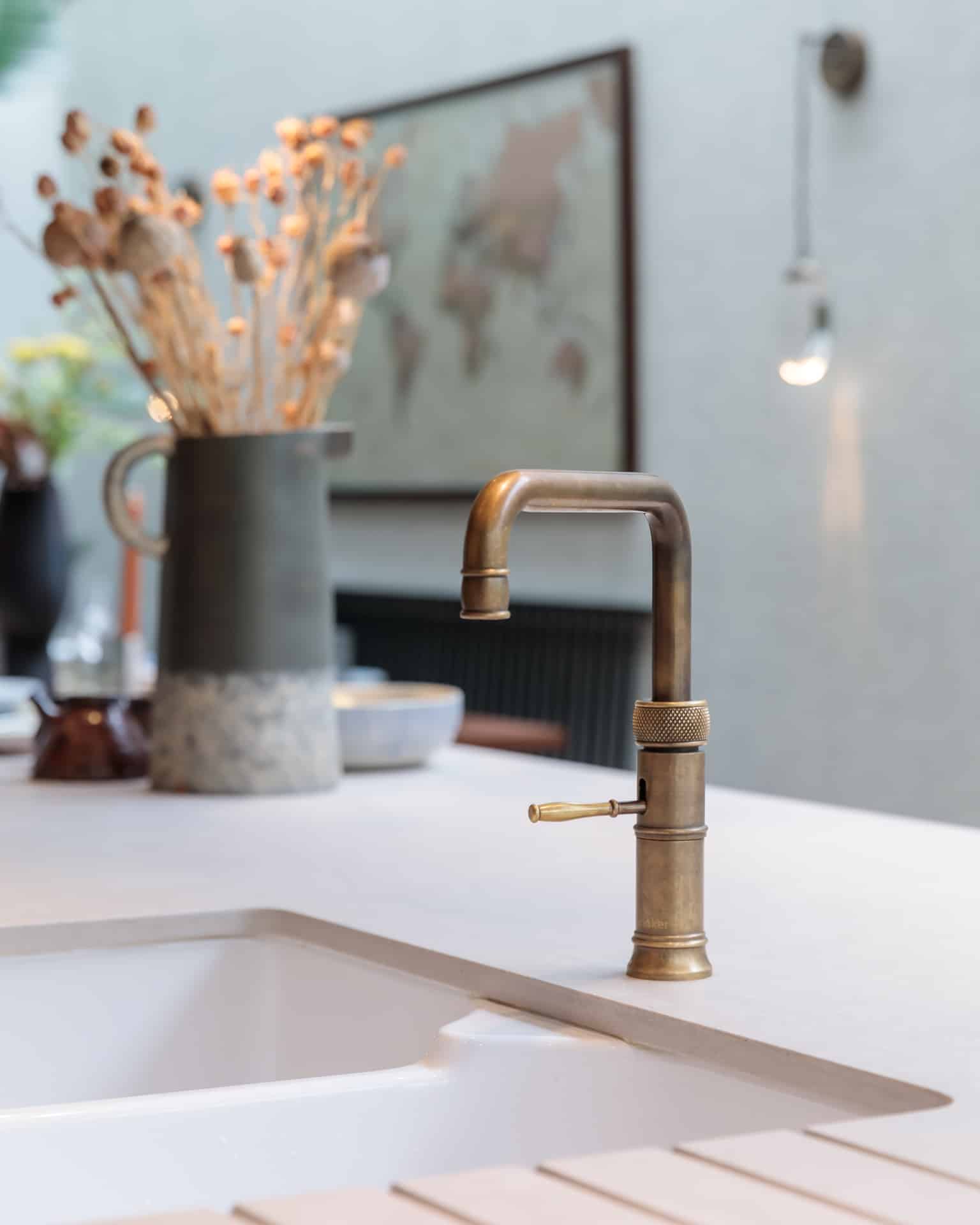 Brass kitchen tap featured prominently on a stylish countertop with a decorative vase and soft lighting in the background, showcasing modern design elements. An Arch KBB team member is present, enhancing the professional atmosphere.