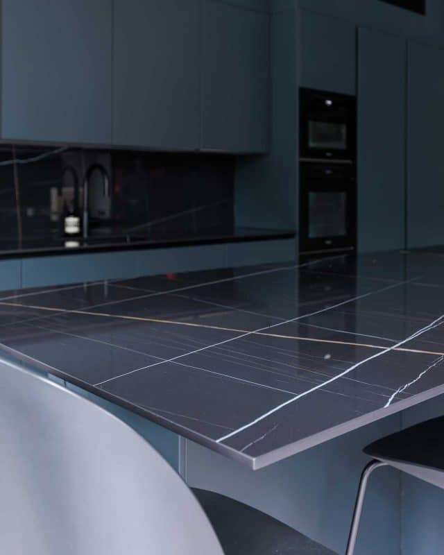 Close-up of a sleek black kitchen countertop with striking white and gold veining, featuring modern cabinetry and appliances in a contemporary kitchen setting, showcasing the design expertise of an Arch KBB team member.