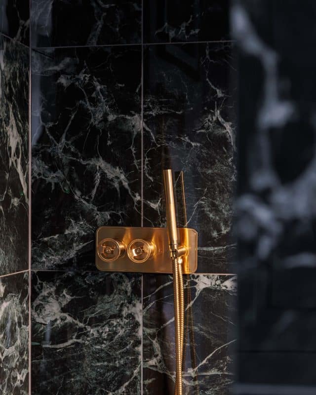 Luxurious shower fixture against a backdrop of dark marble tiles, showcasing a modern design with elegant gold accents, installed by an Arch KBB team member. Ideal for high-end bathroom renovations.