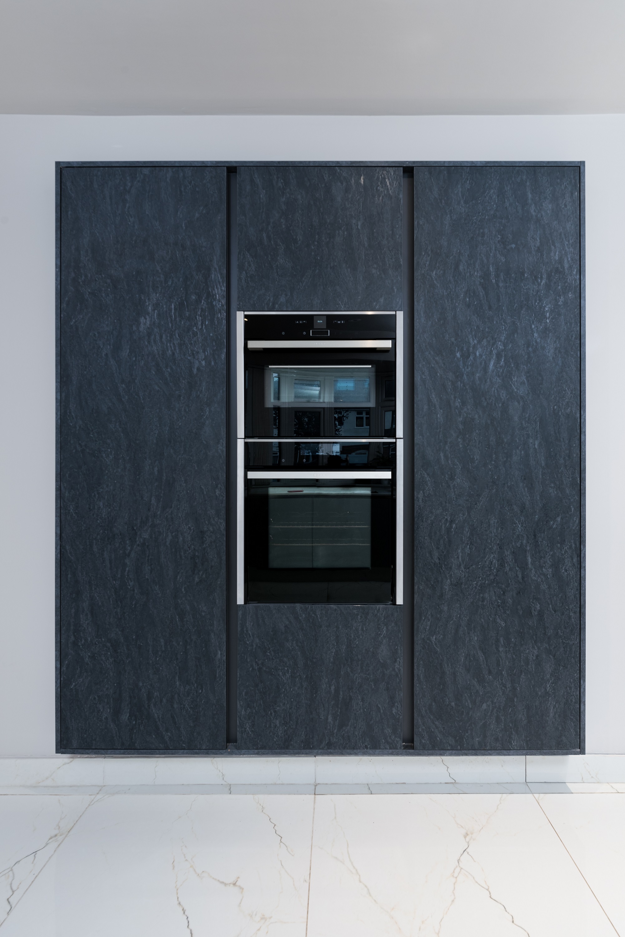 Modern kitchen featuring a built-in double oven with a sleek black finish, surrounded by dark stone cabinetry. An Arch KBB team member is present, showcasing the contemporary design and functionality of the kitchen space.