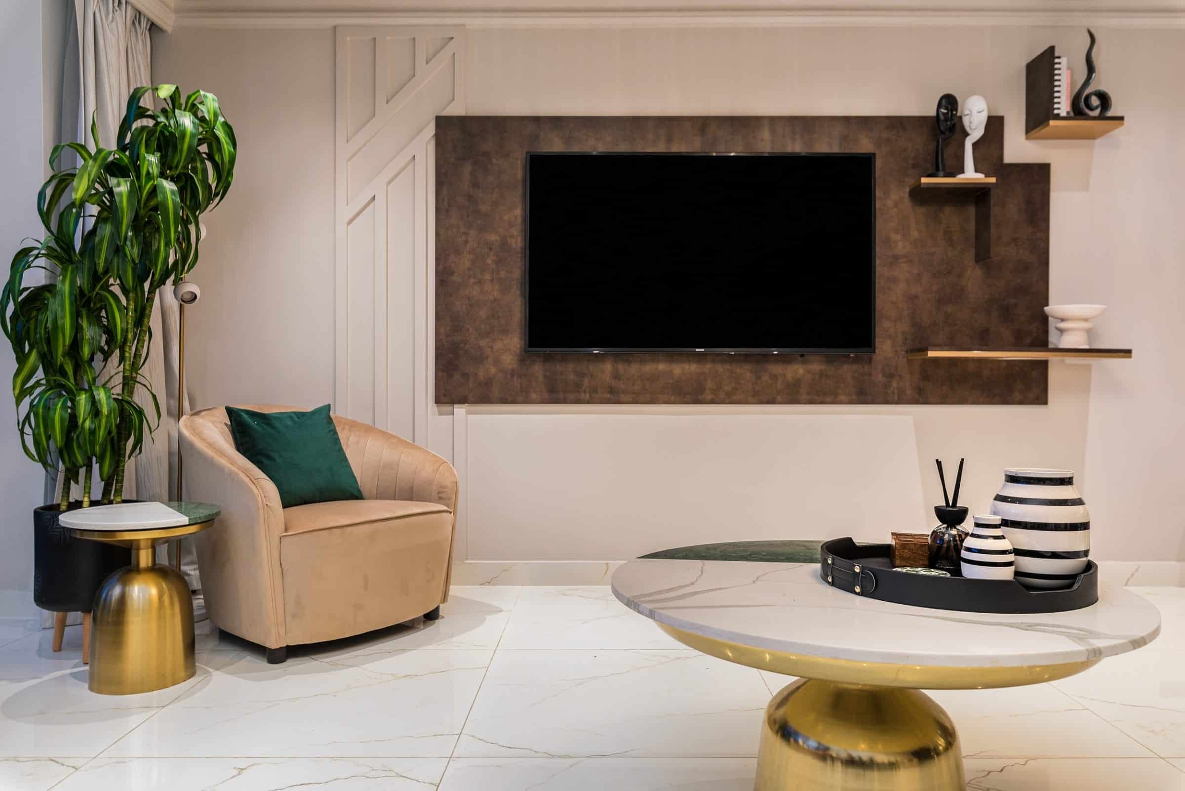 Stylish living room featuring a comfortable armchair, a modern coffee table, and a mounted television against a textured wall. Decorative elements include a large indoor plant and assorted vases, creating a contemporary and inviting atmosphere. An Arch KBB team member is present, contributing to the design's aesthetic.