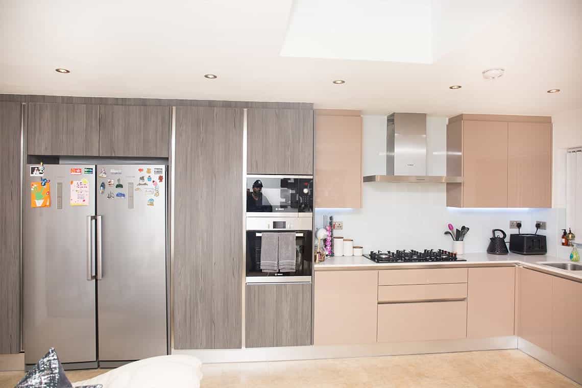 Modern kitchen design featuring sleek cabinetry, a stainless steel fridge, built-in oven, and gas hob. The interior is well-lit with recessed lighting, showcasing a contemporary aesthetic. An Arch KBB team member is present, contributing to the kitchen's design.