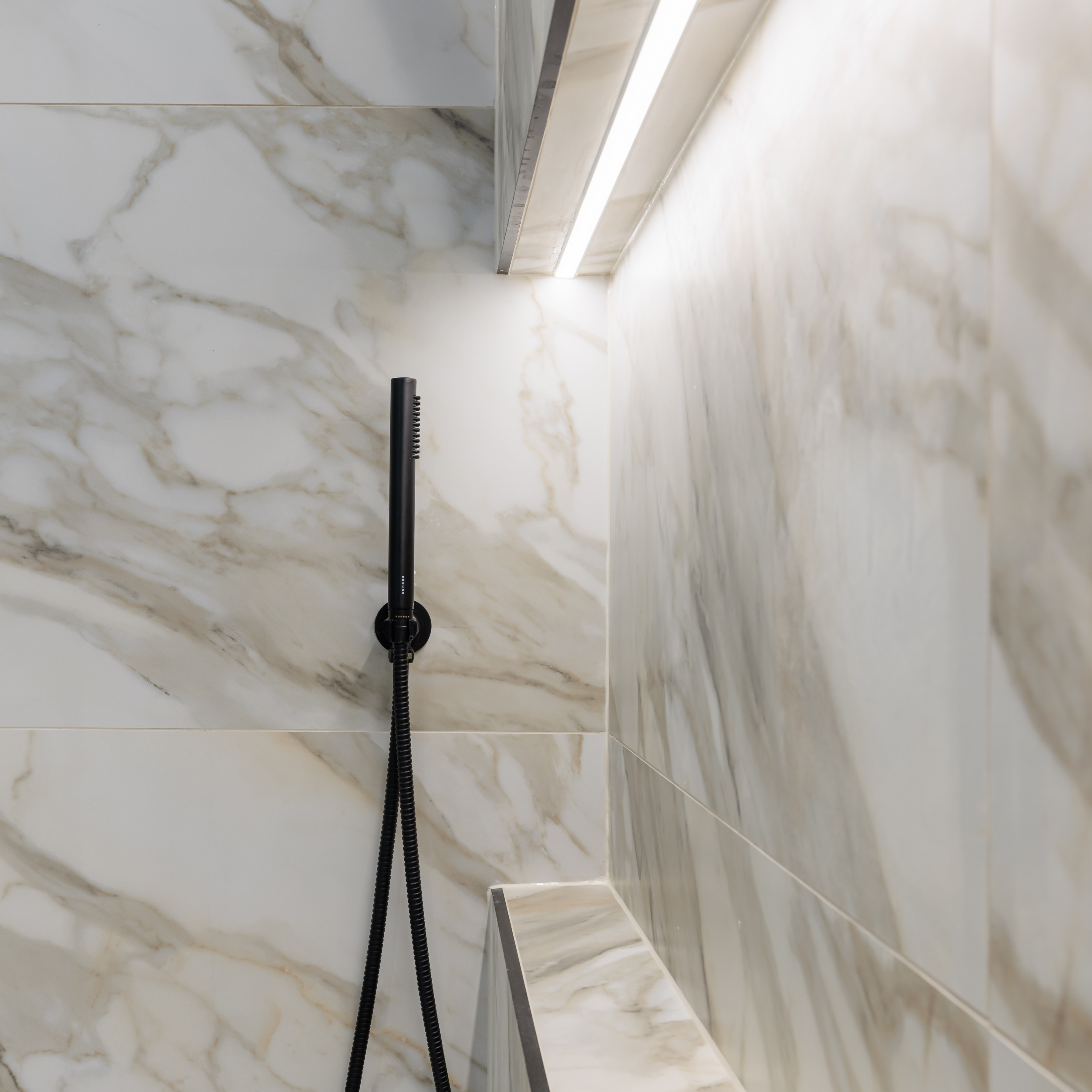 Close-up of a modern bathroom featuring elegant marble walls and a sleek black showerhead, showcasing contemporary design elements. An Arch KBB team member is present, demonstrating attention to detail in the bathroom's aesthetics.