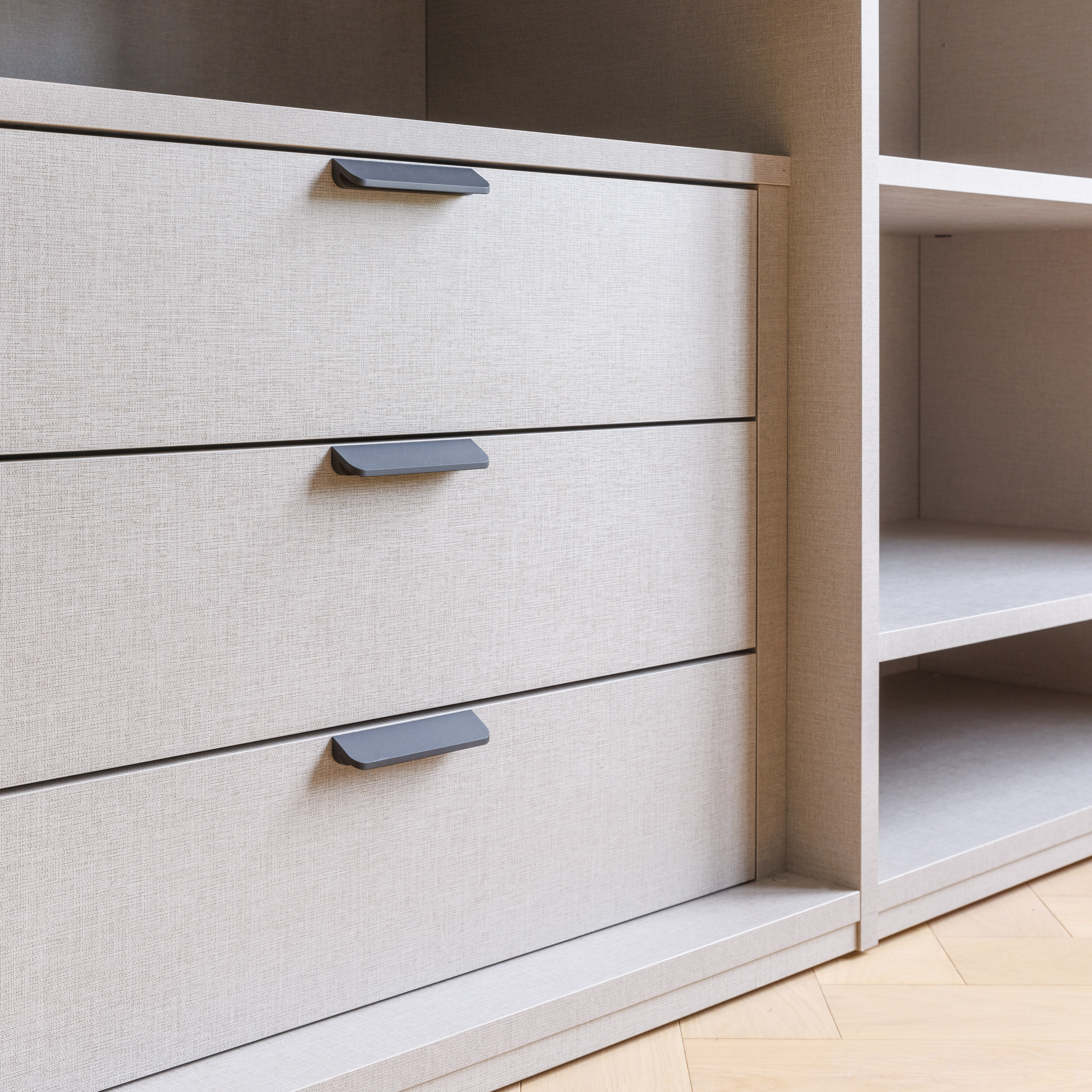 Close-up of a modern storage unit featuring three textured drawers with sleek black handles, showcasing a minimalist design ideal for contemporary interiors. An Arch KBB team member is present, demonstrating the functionality of the furniture.