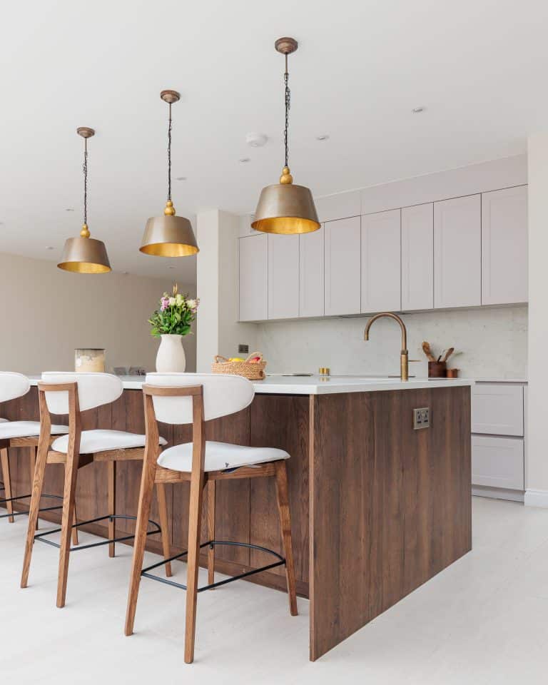 Modern kitchen interior featuring a stylish island with wooden cabinetry, white countertops, and pendant lighting. Arch KBB team member is preparing a floral arrangement on the island, which is complemented by elegant bar stools. The background showcases sleek cabinetry and contemporary design elements, creating a warm and inviting atmosphere.