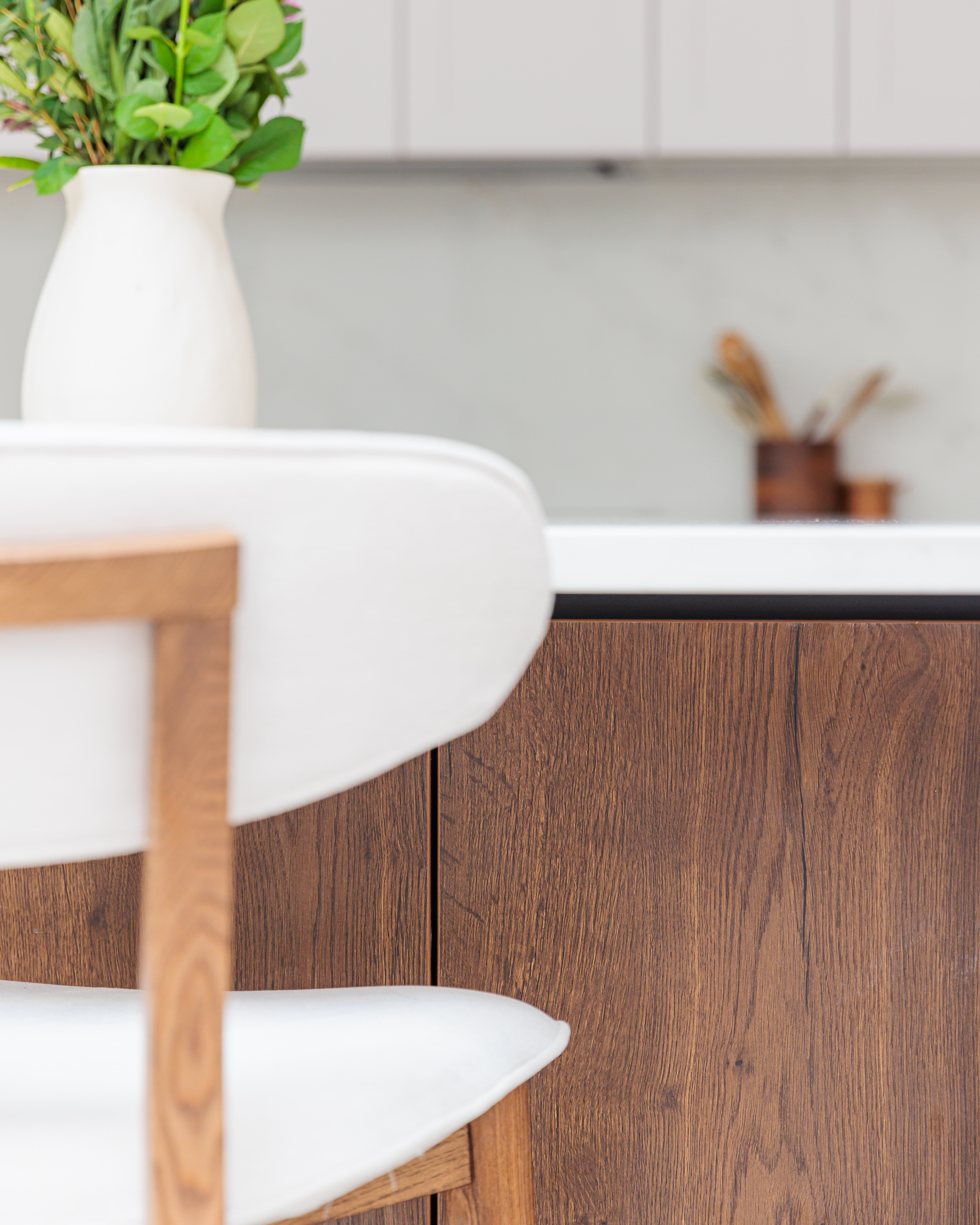 Close-up view of a stylish kitchen featuring a wooden cabinet and a modern chair. The image showcases a minimalist design aesthetic with a focus on natural materials, enhancing the overall contemporary feel of the space. An Arch KBB team member is present, contributing to the design process.