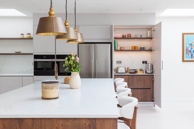 Modern kitchen with large white island, wooden accents, pendant lights, and integrated appliances, showcasing a stylish and functional design.
