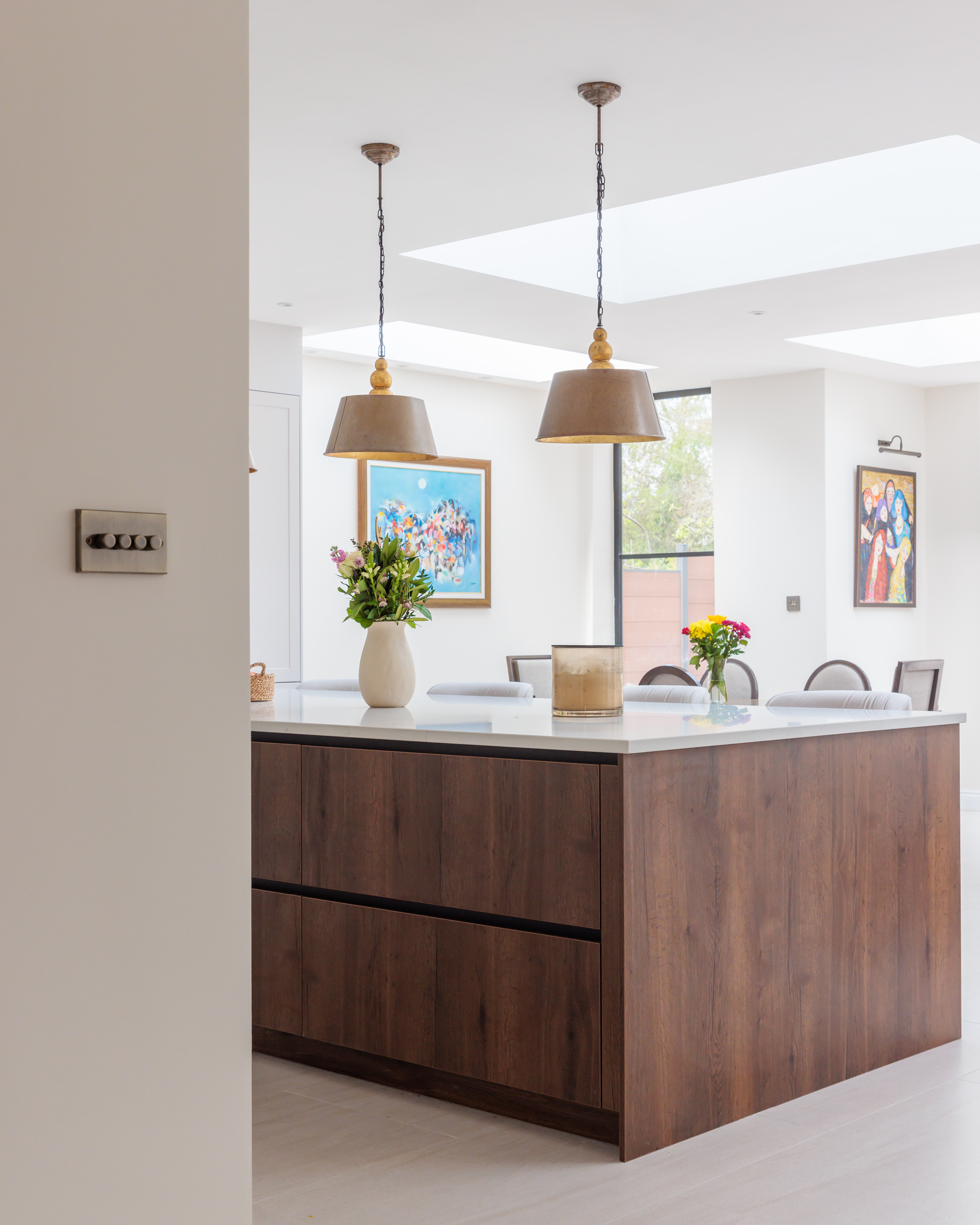 Modern kitchen interior featuring a stylish island with wooden cabinetry, decorative pendant lights, and vibrant flower arrangements. Artwork adorns the walls, enhancing the contemporary design. An Arch KBB team member is present, contributing to the inviting atmosphere.