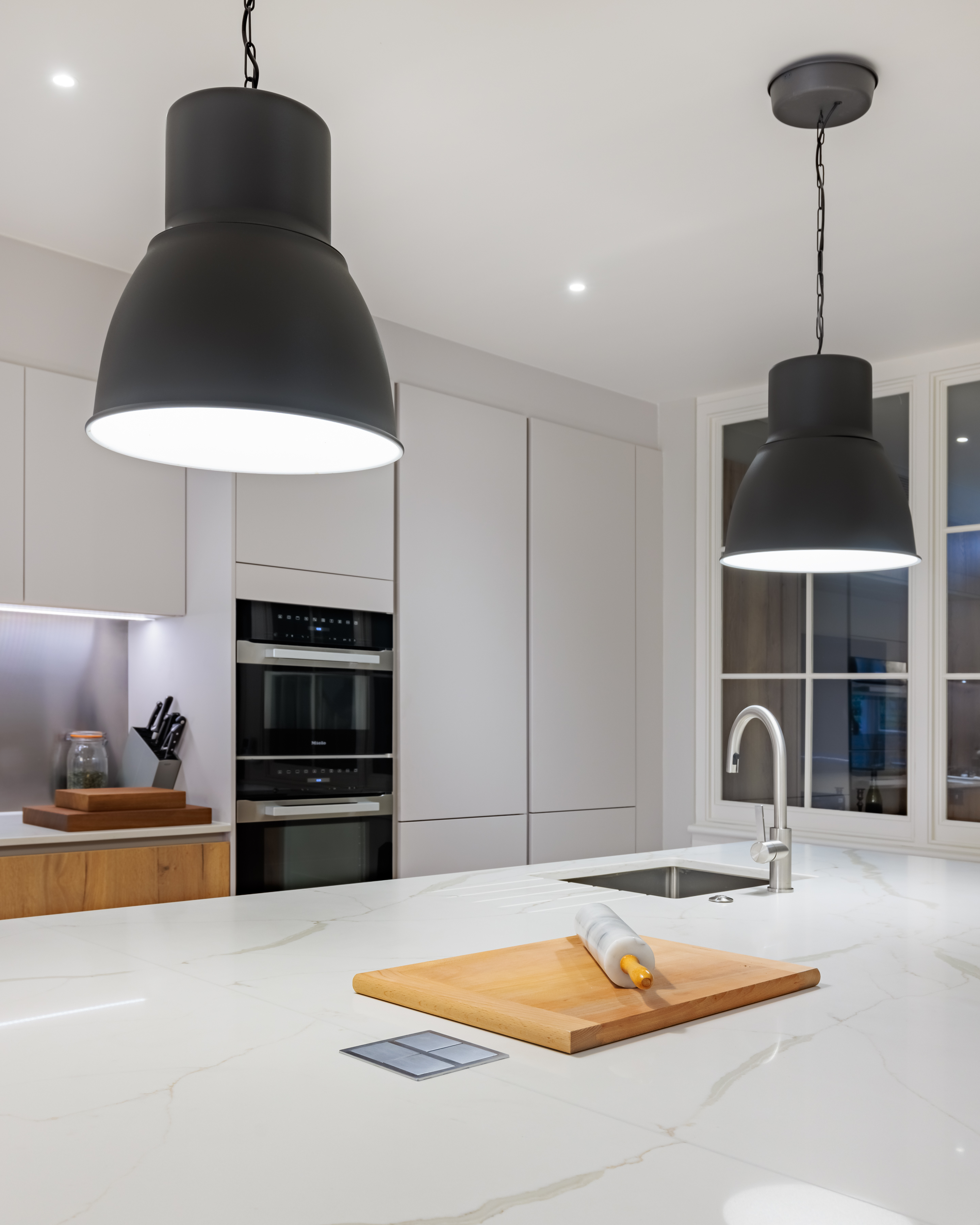 Modern kitchen featuring sleek cabinetry, integrated appliances, and a stylish island with a sink. Two black pendant lights illuminate the space, enhancing the contemporary design while an Arch KBB team member is present, contributing to the kitchen's ambience.