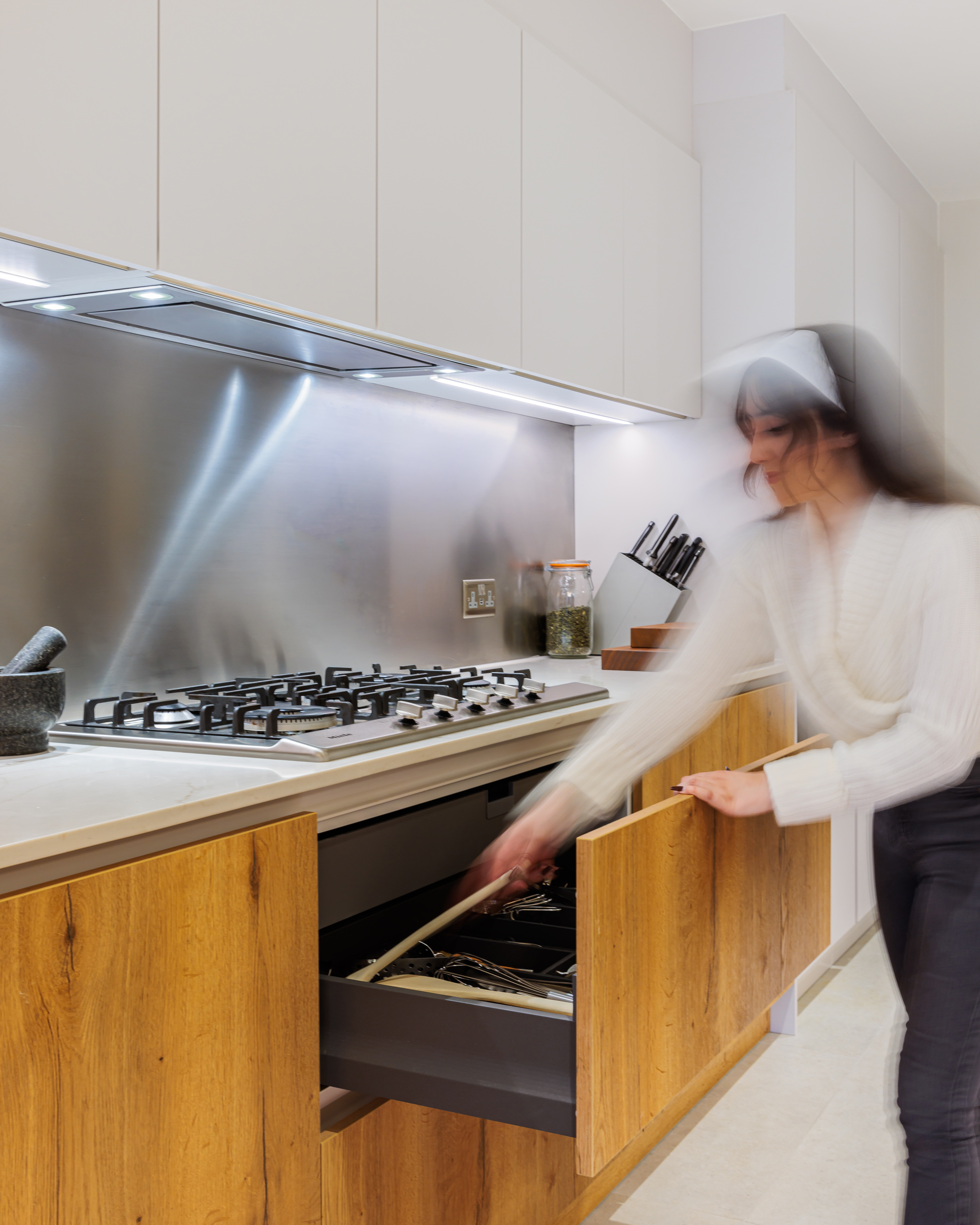 Arch KBB team member organising kitchen drawers in a modern kitchen with stainless steel appliances and wooden cabinetry, showcasing a sleek and functional design.