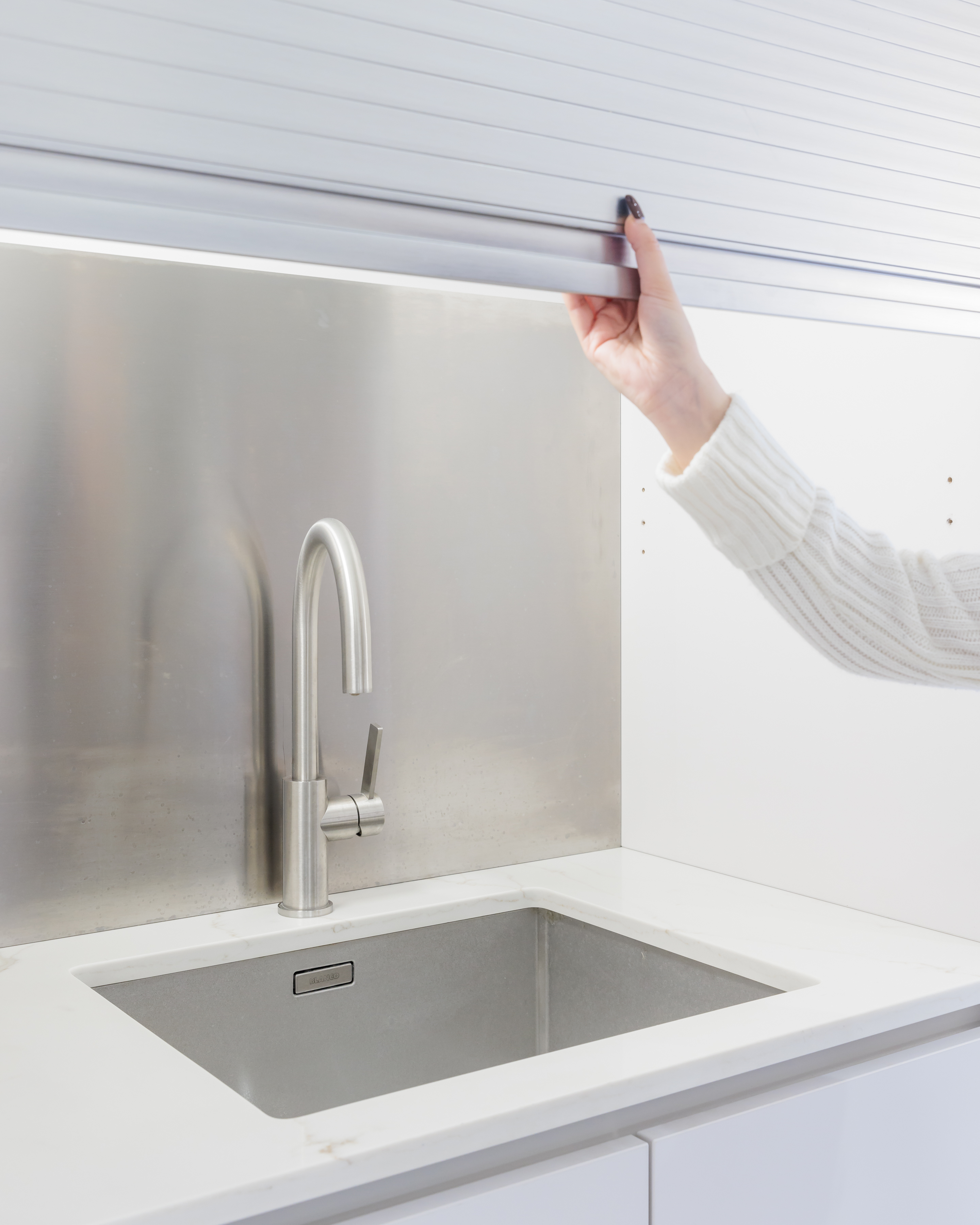 Arch KBB team member adjusting a modern kitchen tap in a stylish, minimalistic kitchen setting with a stainless steel splashback and a sleek sink.
