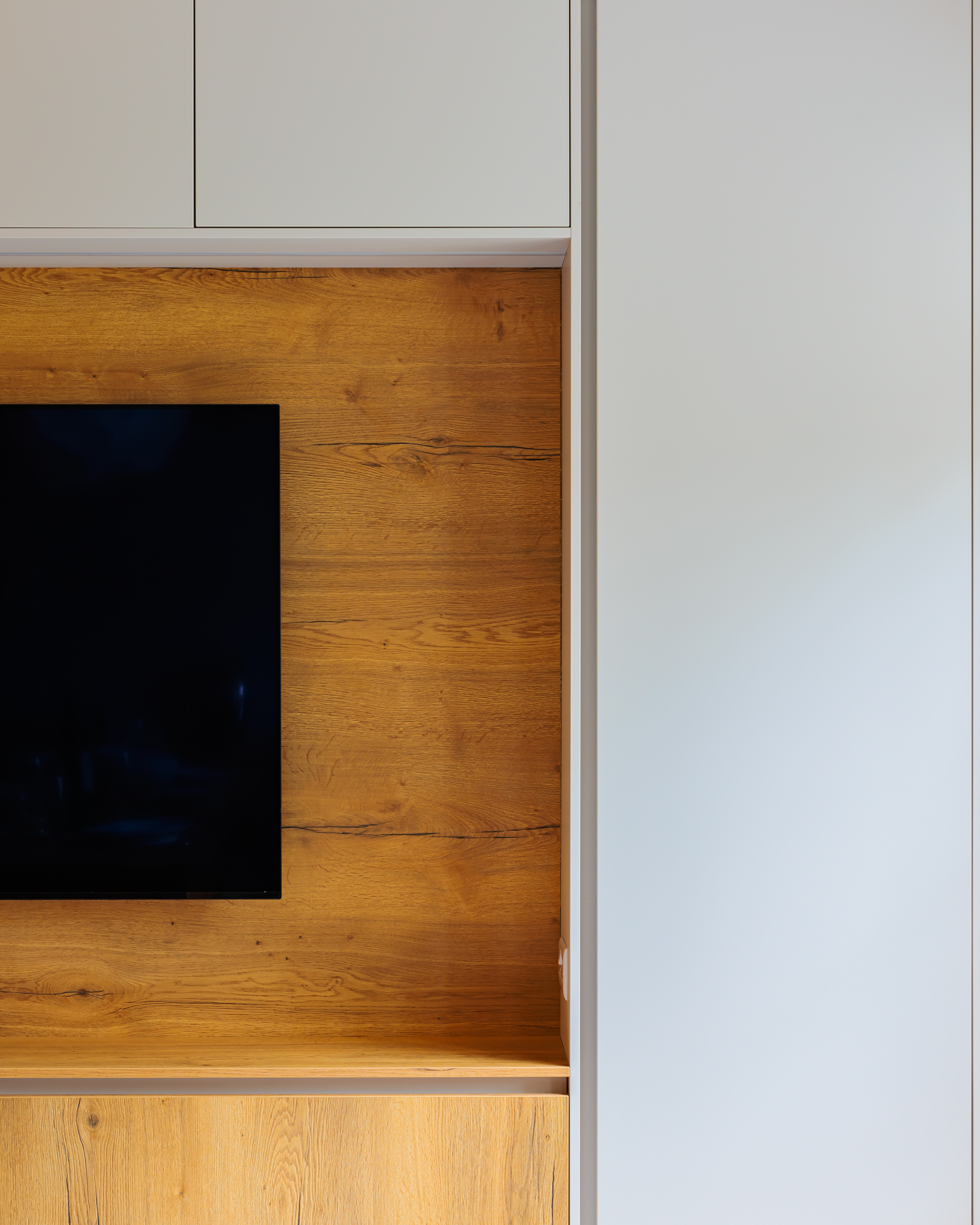 A modern living space featuring a sleek, wall-mounted television against a textured wooden wall. The design combines natural elements with contemporary aesthetics, showcasing a stylish and minimalistic interior. An Arch KBB team member is present, contributing to the ambiance of the room.