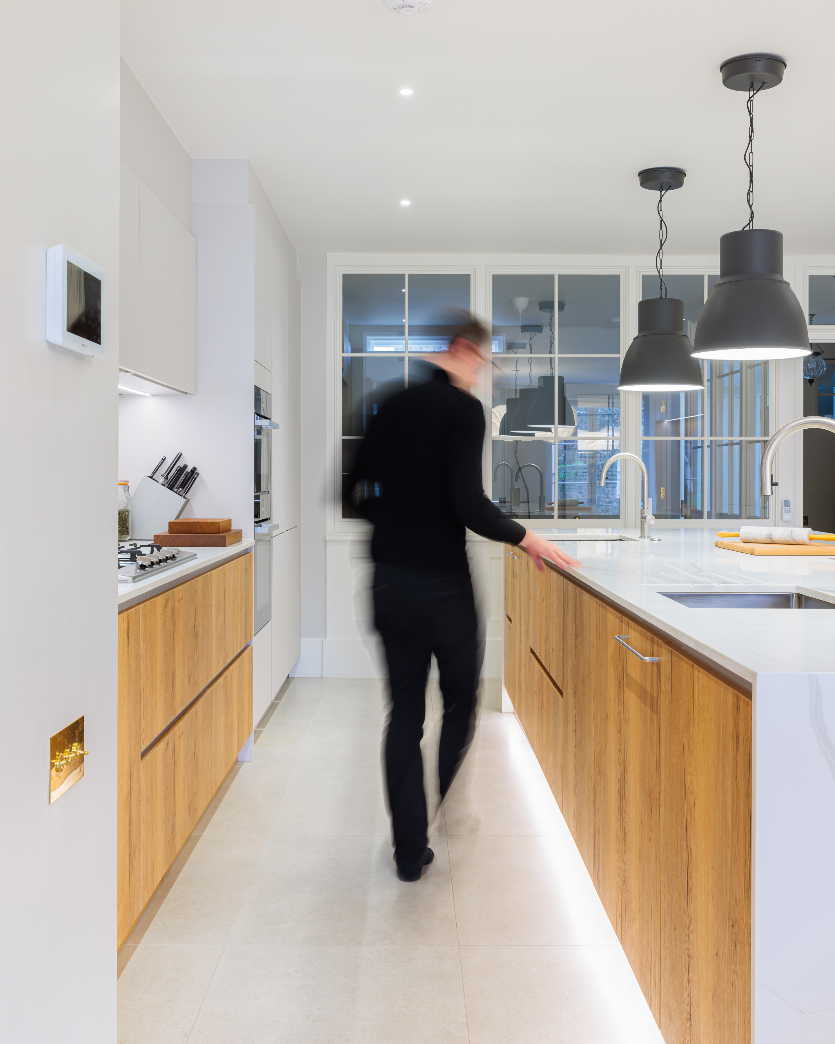 Modern kitchen design featuring wooden cabinetry and sleek countertops, with an Arch KBB team member interacting within the space. The room is well-lit, showcasing contemporary fixtures and a functional layout.
