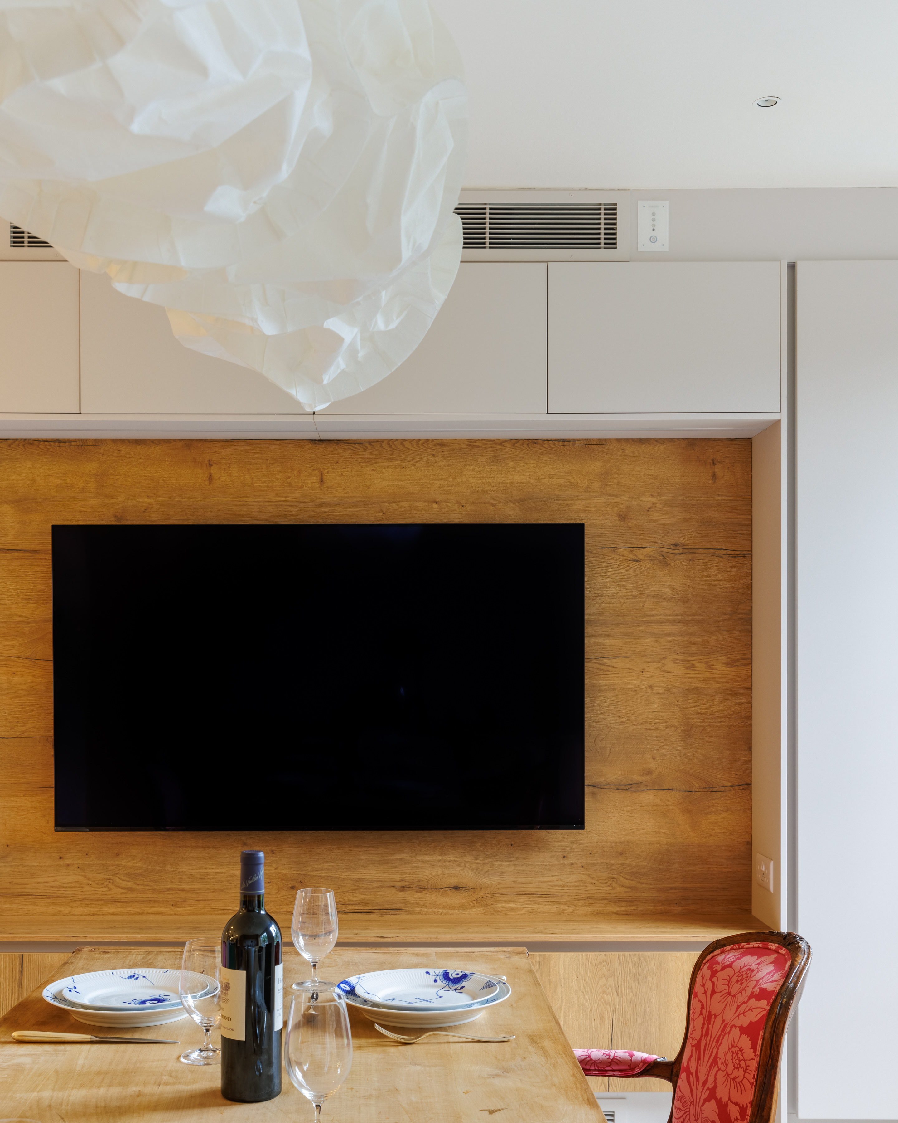 Modern living room featuring a large flat-screen television mounted on a wooden accent wall, complemented by sleek cabinetry and a contemporary light fixture. An Arch KBB team member is present, contributing to the stylish interior design.