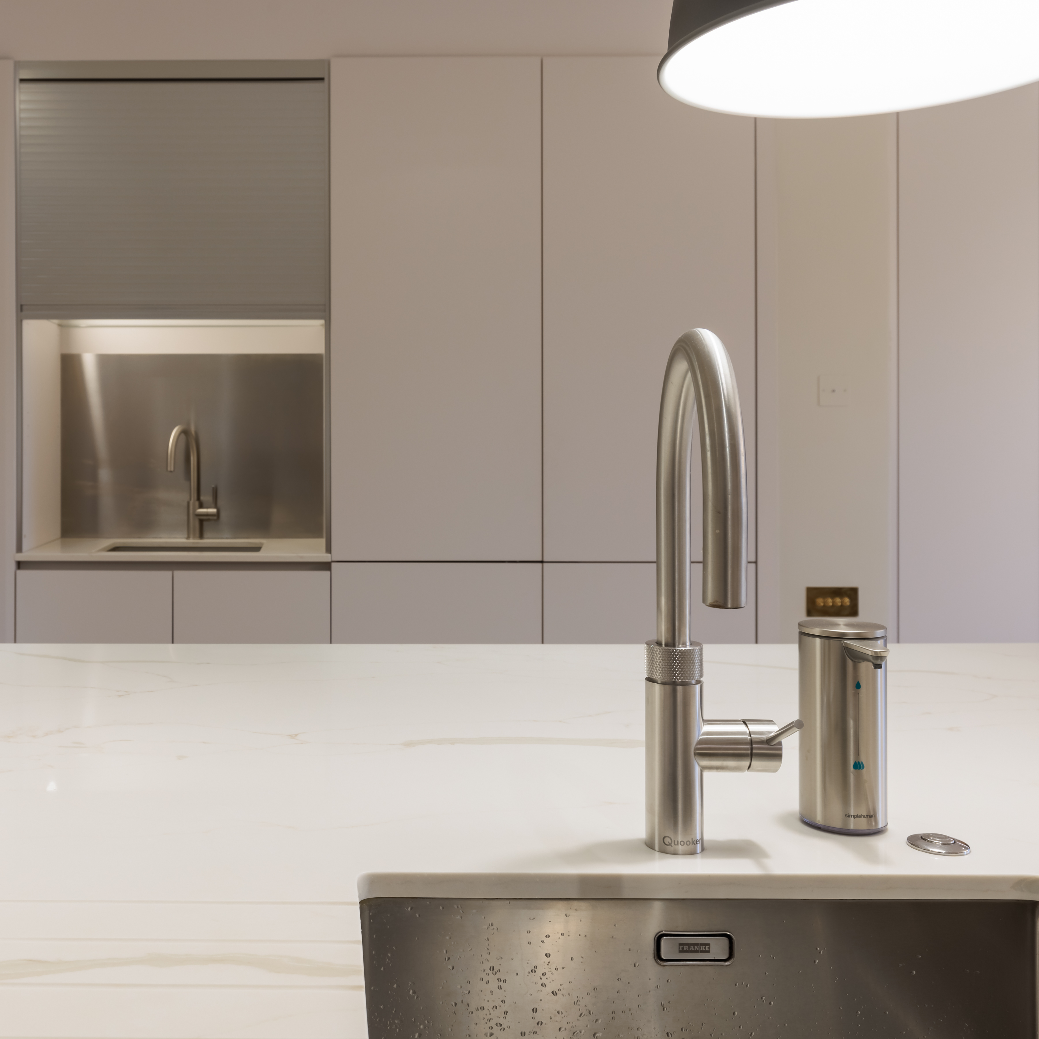 Modern kitchen with a sleek stainless steel tap and a minimalist design. An Arch KBB team member is present, showcasing the contemporary cabinetry and integrated sink in the background. The image highlights the clean lines and functionality of the kitchen space.