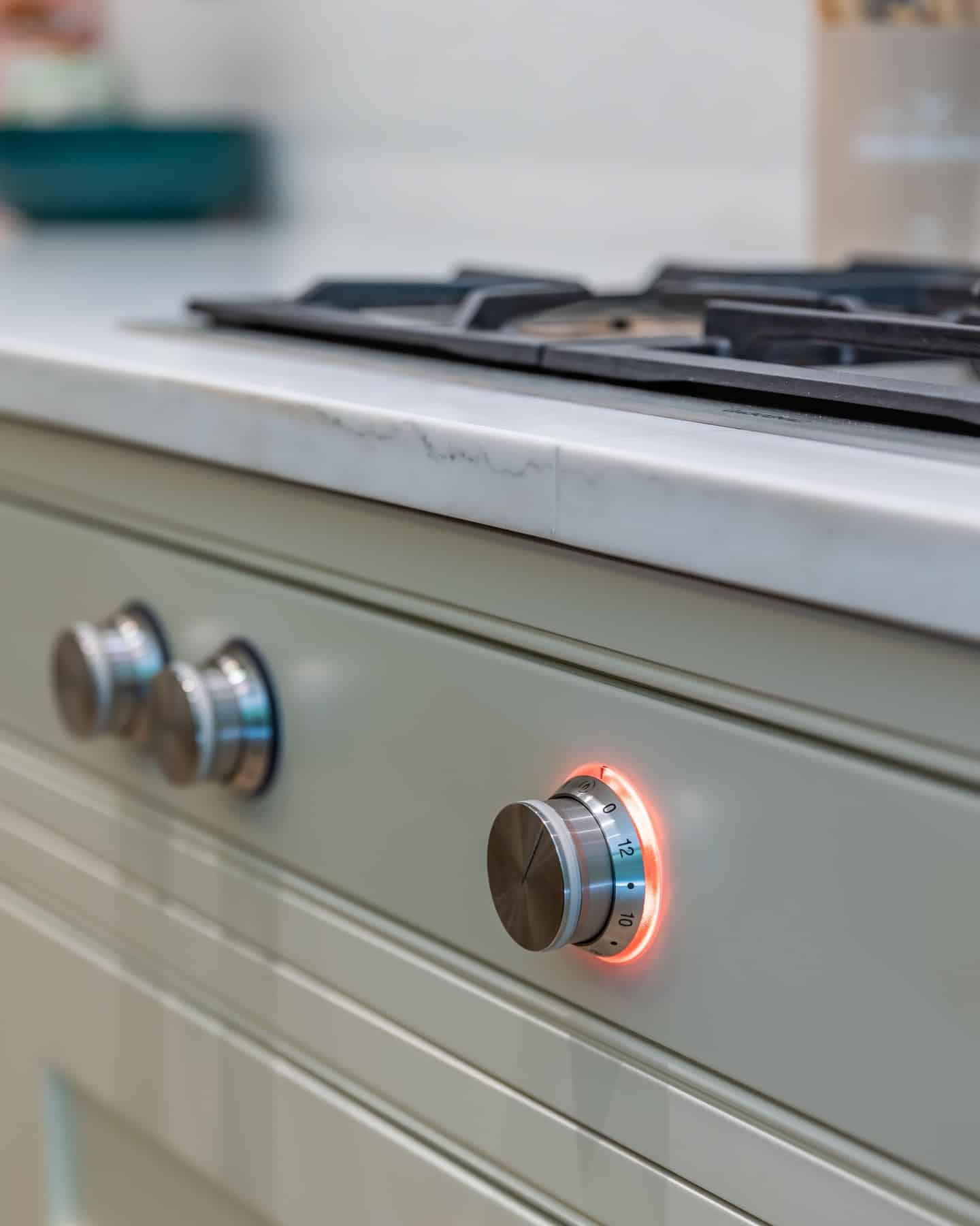 Close-up of a modern kitchen gas stove with illuminated control knobs set against a sleek marble countertop, showcasing the elegant design and functionality of high-quality kitchen appliances. An Arch KBB team member is present, highlighting the expertise in kitchen design.