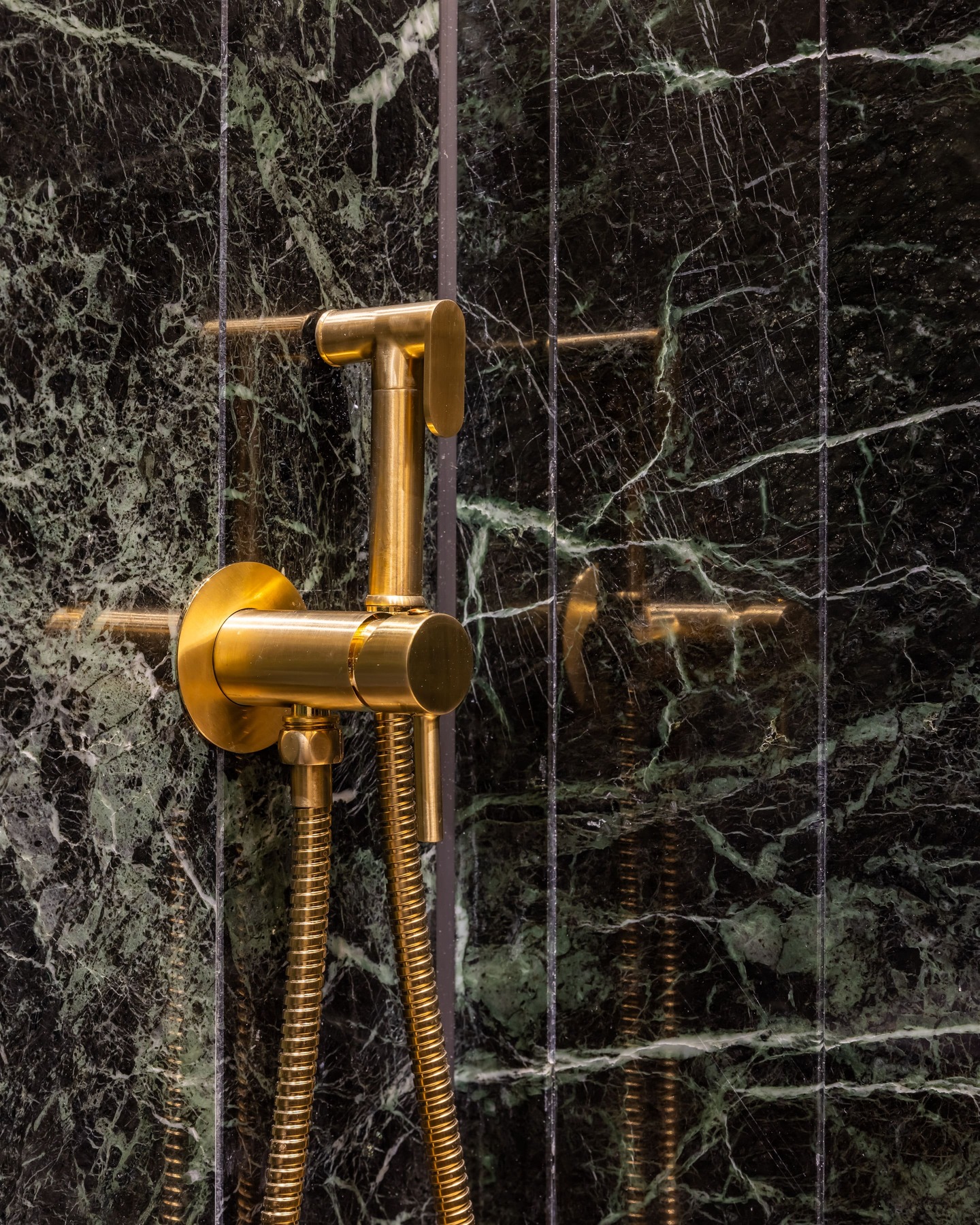 Close-up of a luxurious gold shower fixture mounted on a polished green marble wall, showcasing modern bathroom design elements. An Arch KBB team member is present, contributing to the installation.