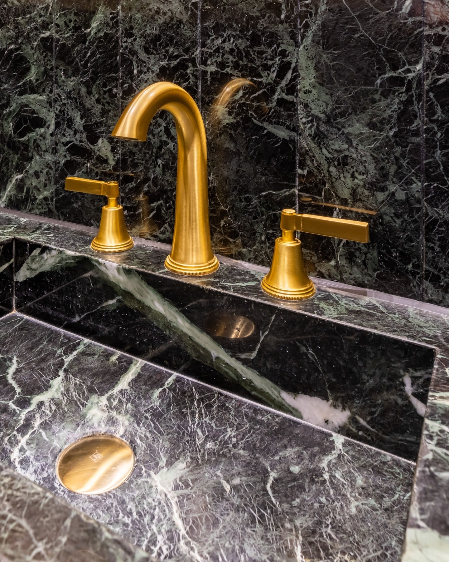 Close-up of a luxurious bathroom sink featuring a striking black marble countertop with green veining, complemented by elegant gold taps. The design showcases a modern aesthetic, perfect for upscale interior spaces. An Arch KBB team member is present, enhancing the tailored experience of the setting.