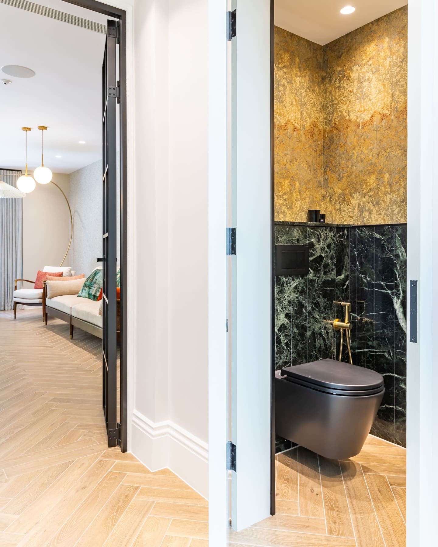 Modern interior design featuring a stylish bathroom with black marble walls and gold accents. An Arch KBB team member stands near the entrance, showcasing the elegant transition between the bathroom and living area, highlighted by contemporary furniture and lighting.