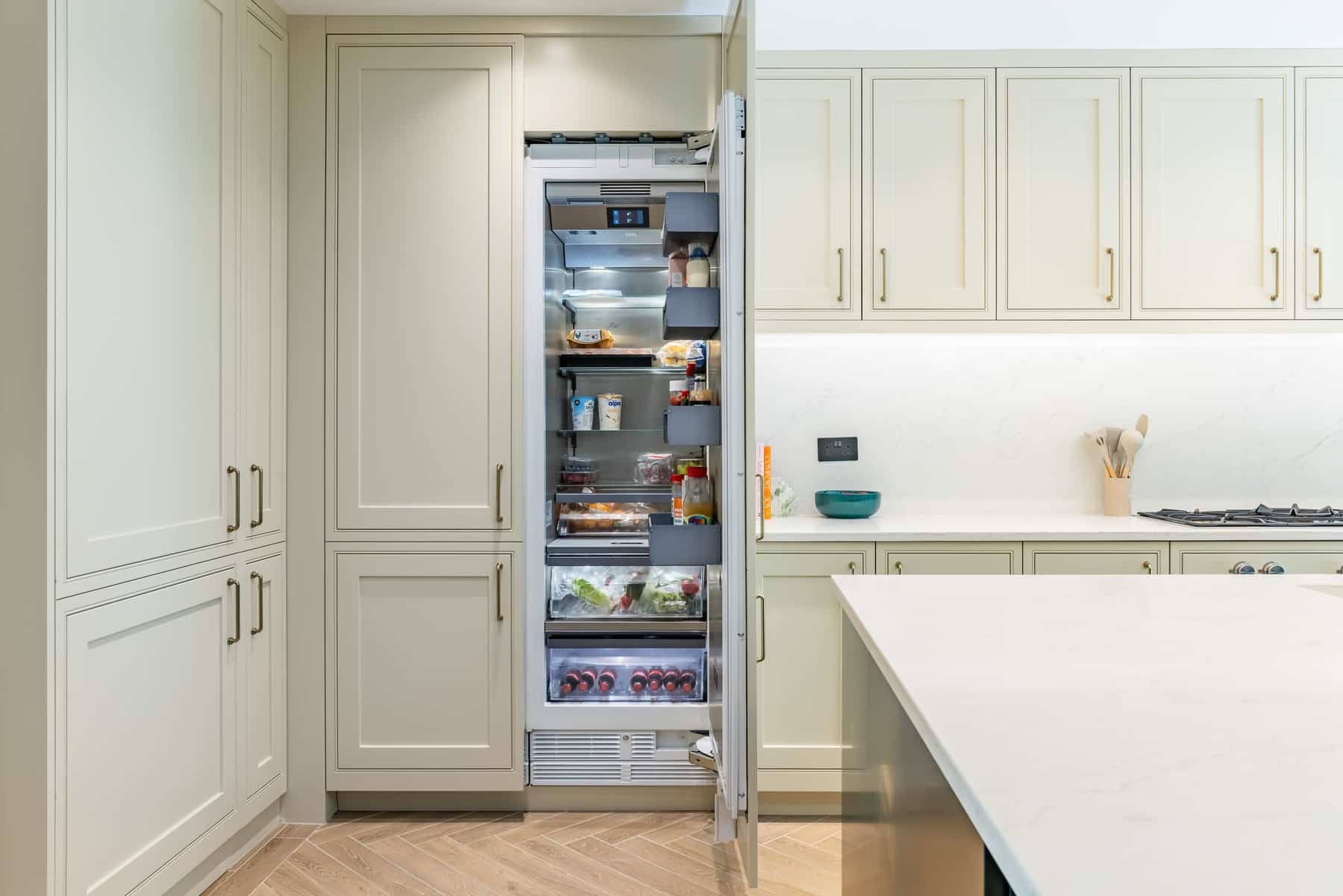 Modern kitchen featuring an open fridge filled with organised food items, surrounded by stylish cabinetry and a sleek countertop. An Arch KBB team member is present, showcasing the kitchen design.