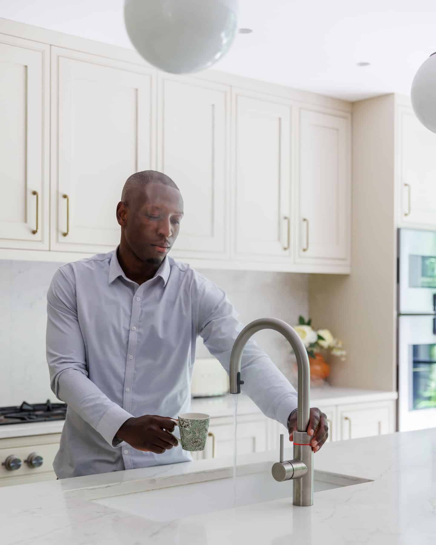Arch KBB team member preparing a hot beverage in a modern kitchen, with steam rising from the tap and stylish cabinetry in the background.