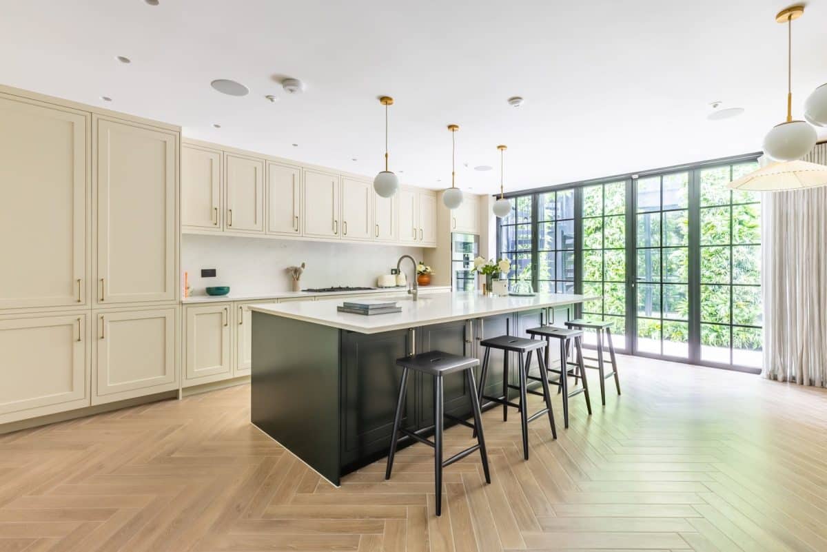 Modern kitchen featuring elegant cabinetry, a spacious island with seating, and large windows allowing natural light. An Arch KBB team member is present, showcasing the stylish interior design and functional layout.