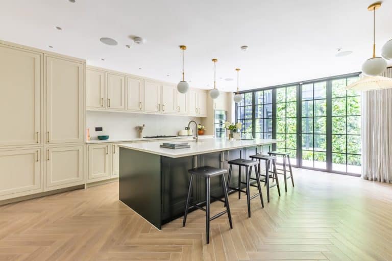 Modern kitchen featuring elegant cabinetry, a spacious island with seating, and large windows allowing natural light. An Arch KBB team member is present, showcasing the stylish interior design and functional layout.
