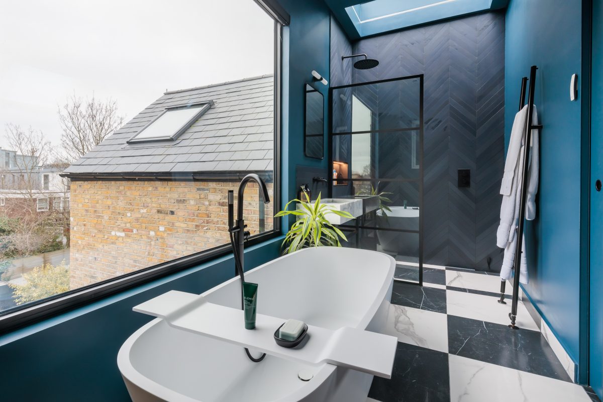 Modern bathroom featuring a freestanding bathtub, large windows for natural light, and a sleek black and white checkered floor. The walls are painted in a rich blue hue, complemented by a stylish shower area with a glass partition and contemporary fixtures. A touch of greenery adds a fresh element to the space.