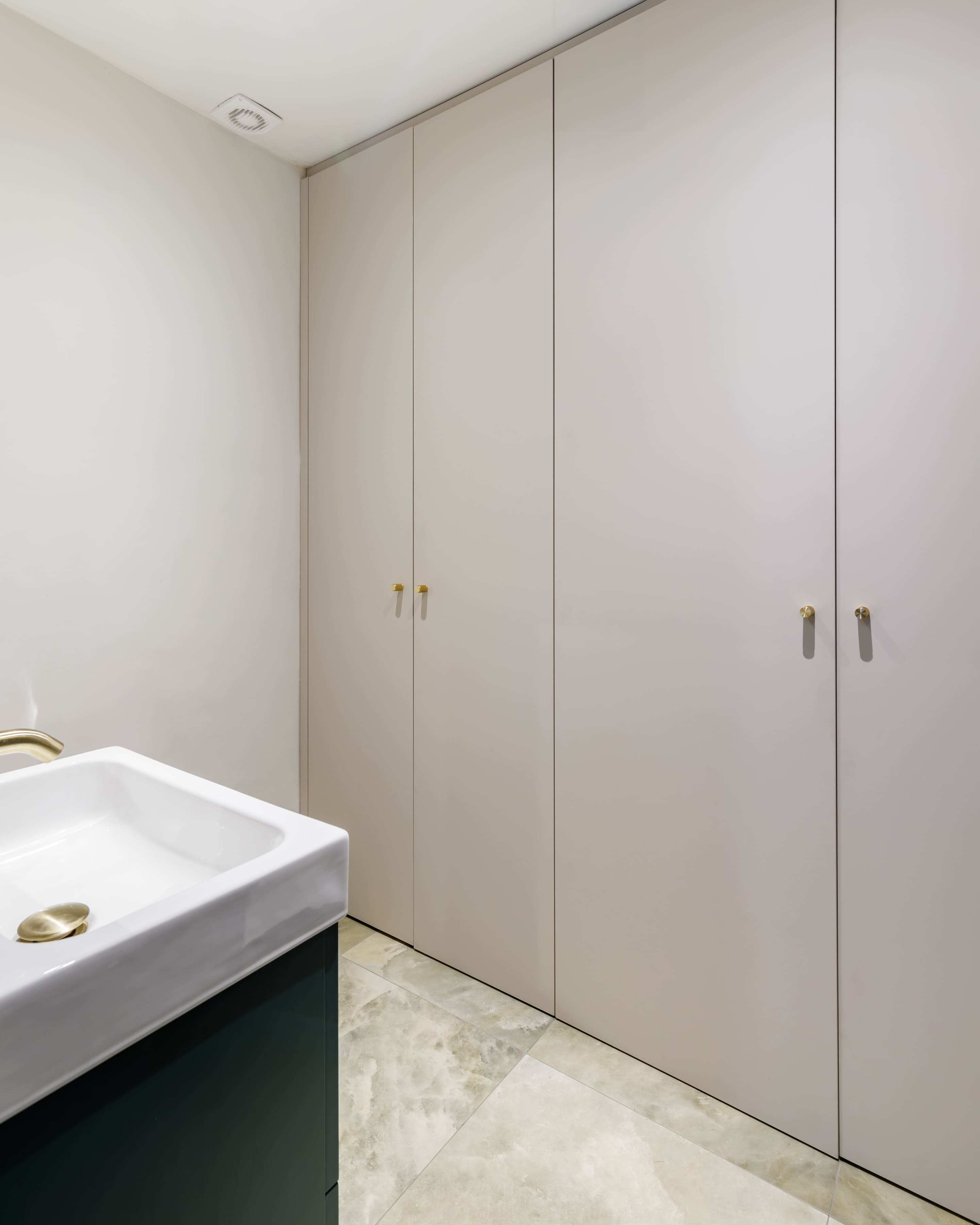 Modern bathroom interior featuring a white sink with a gold tap, complemented by sleek, light-coloured cabinetry with gold handles. The design emphasizes minimalism and functionality, creating a spacious and elegant atmosphere.
