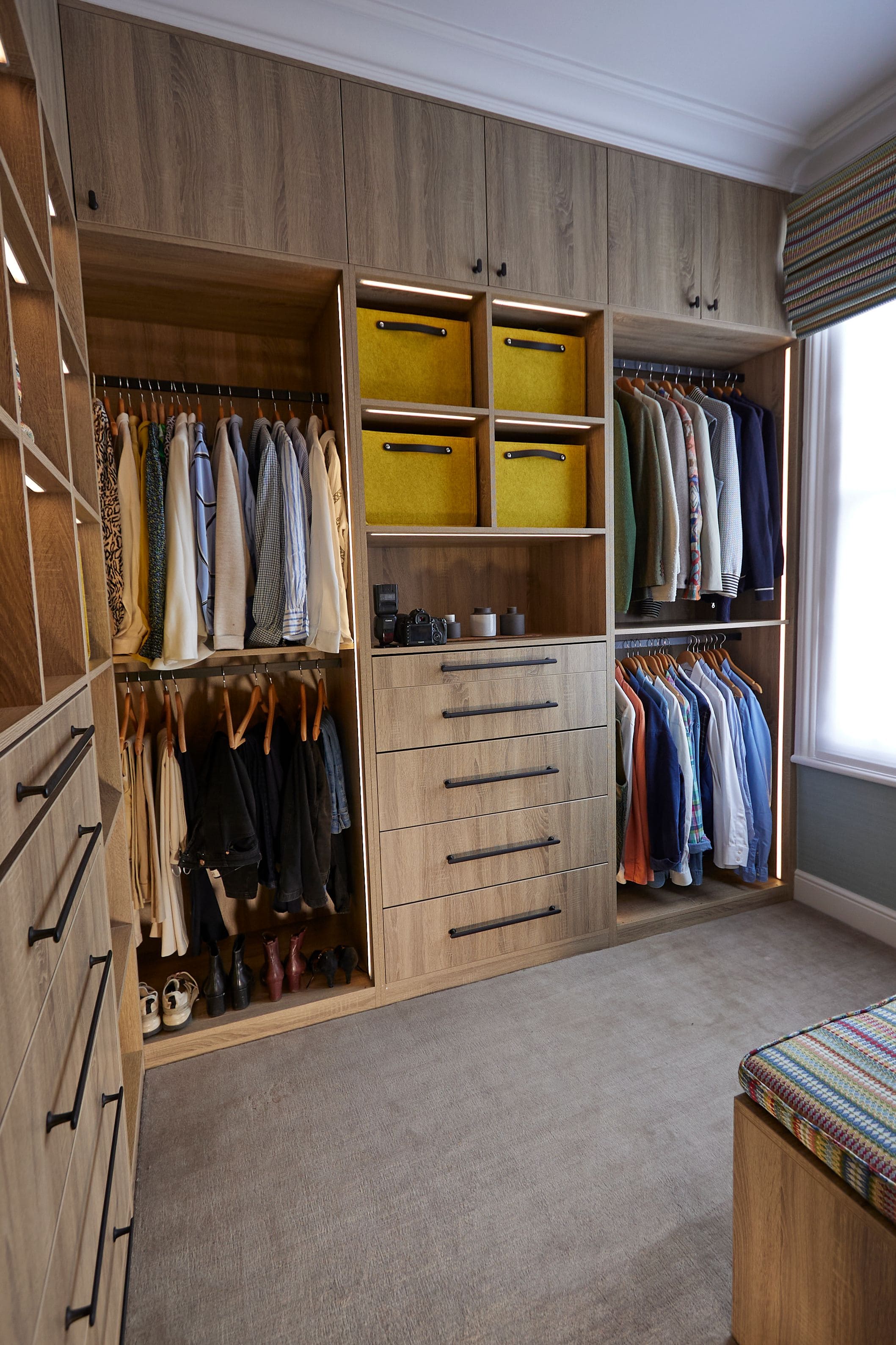 Stylish and organised wardrobe featuring neatly hung clothing, a set of drawers, and storage boxes. The design includes a mix of casual and formal attire, showcasing a well-arranged space for efficient clothing management.
