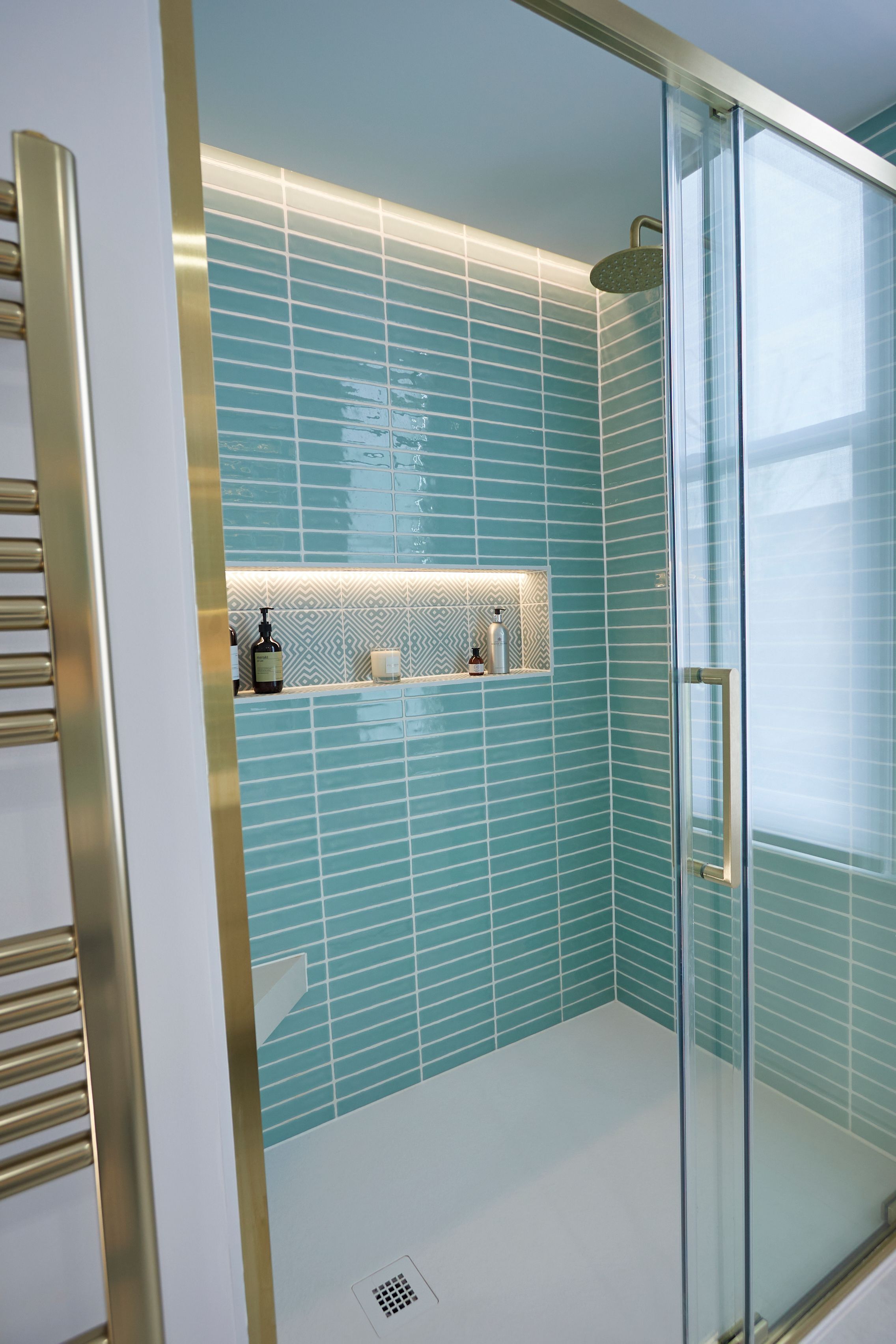 Modern bathroom shower featuring turquoise glazed tiles, a recessed shelf with decorative items, and a sleek glass door. The warm lighting accentuates the geometric pattern on the shelf, creating a stylish and inviting space.
