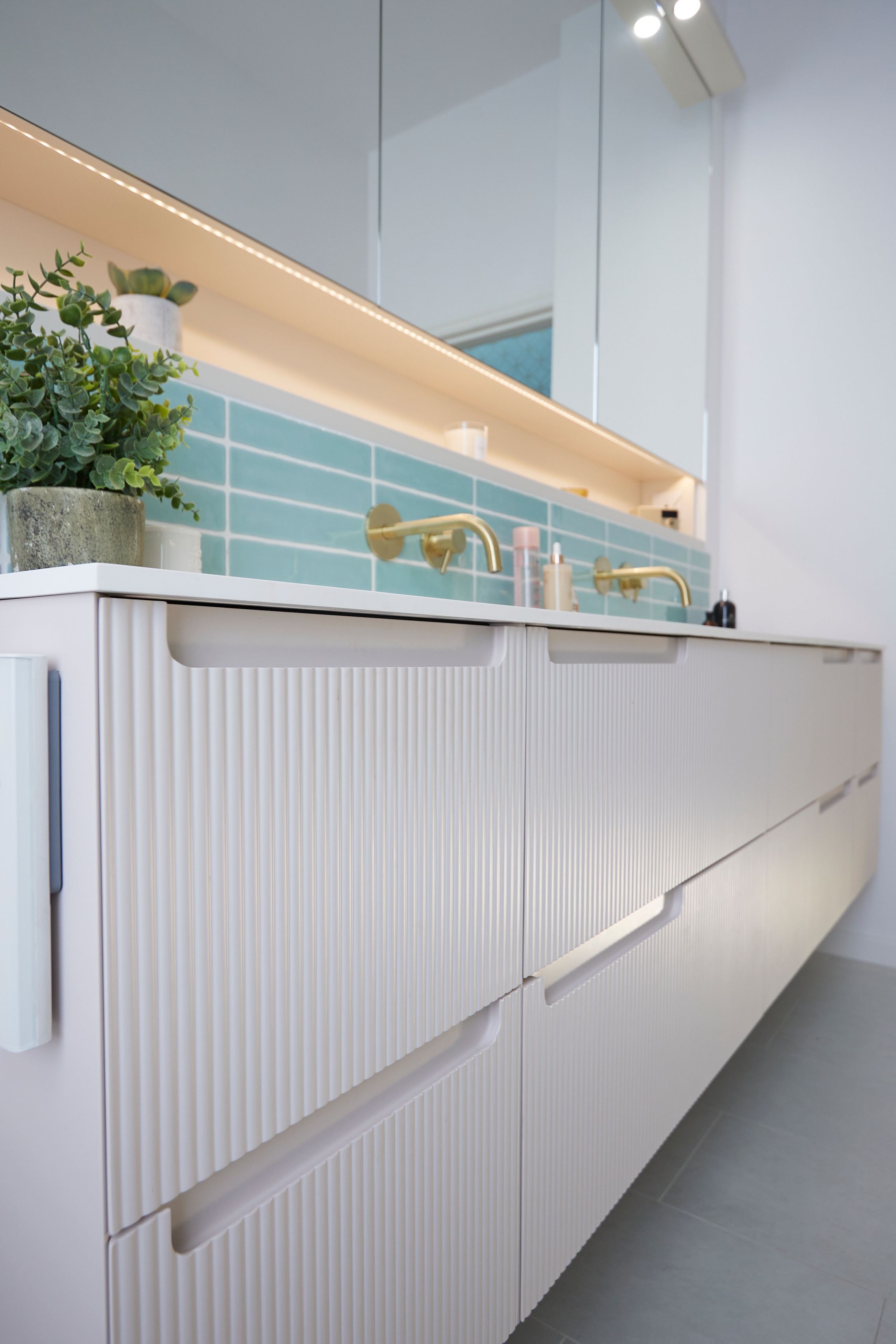 Modern bathroom vanity with ribbed cabinetry, stylish gold faucets, and a turquoise tiled backsplash, featuring a small potted plant for added decor.